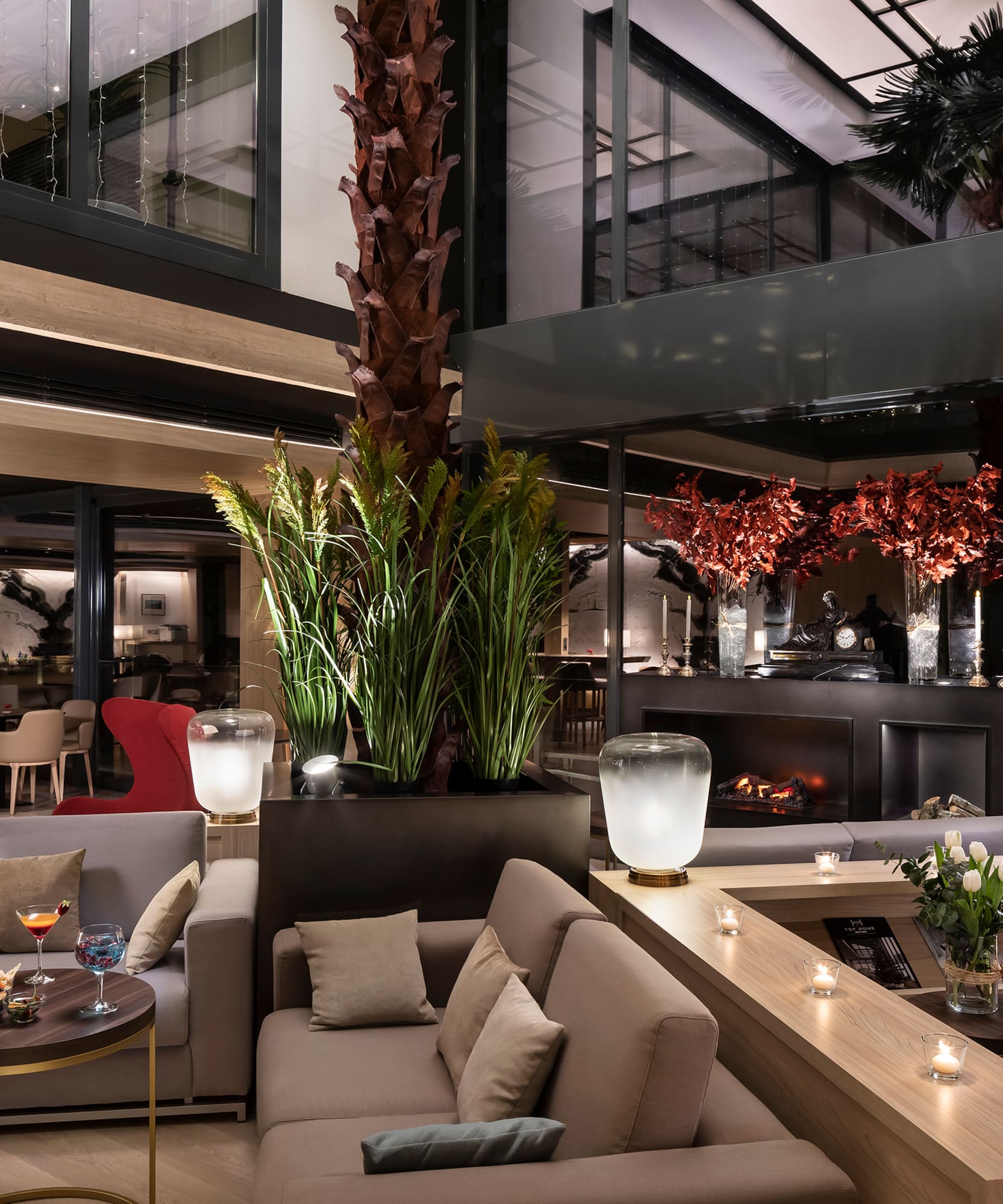 Luxury hotel lounge with modern sofas, fireplace, cocktails, and indoor plants.