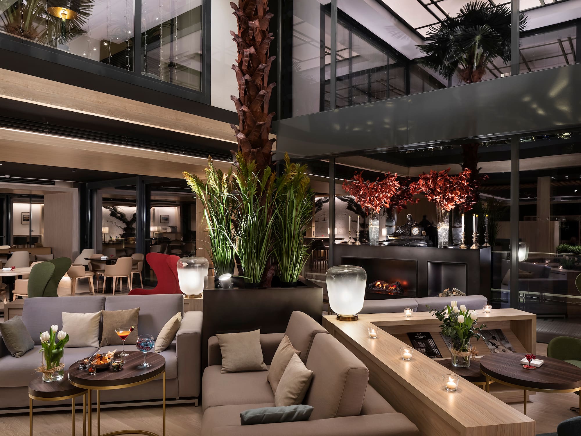 Modern hotel lounge with comfortable sofas, fireplace, cocktails, and palm trees.
