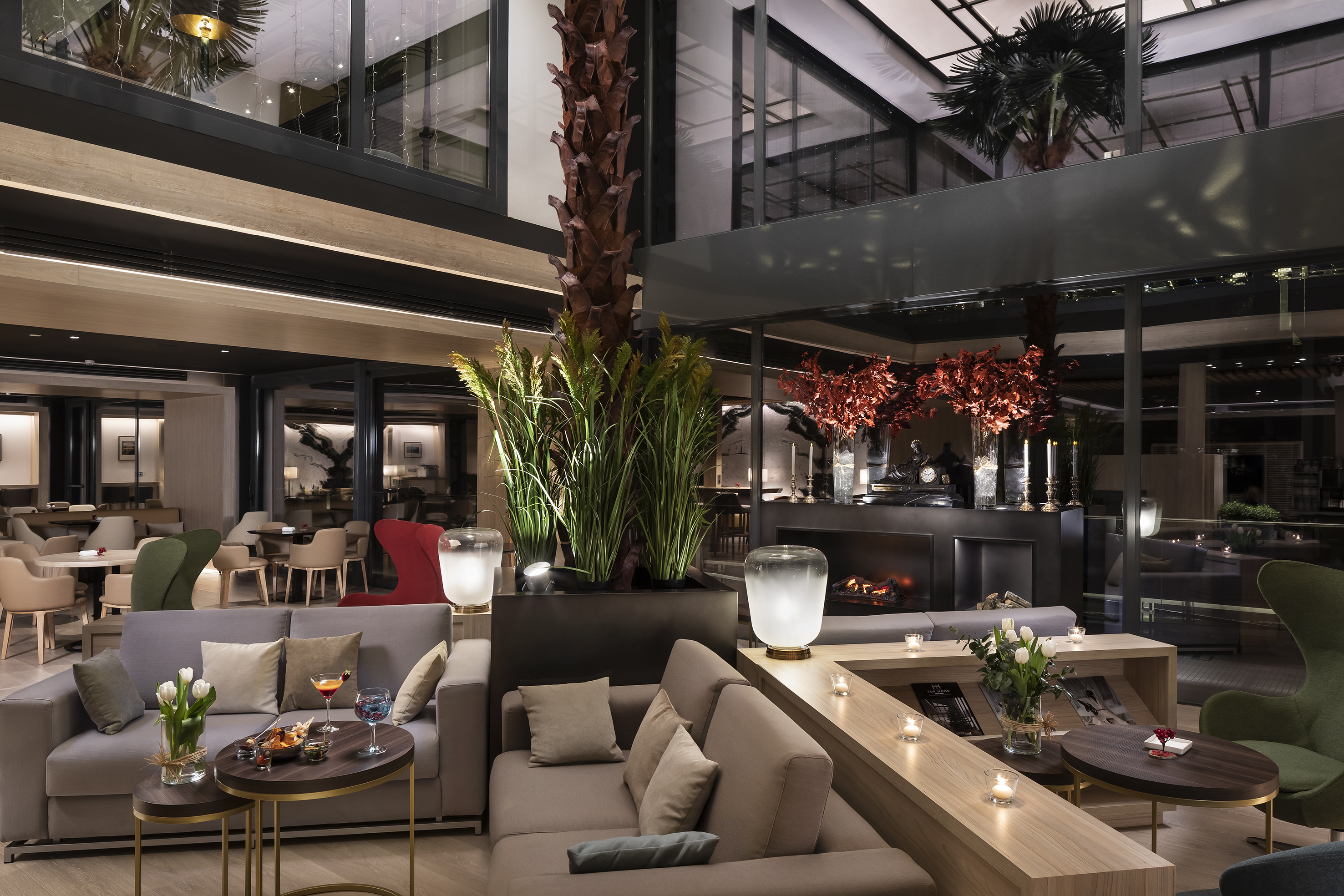 Luxury hotel lounge with modern sofas, fireplace, cocktails, and indoor plants.