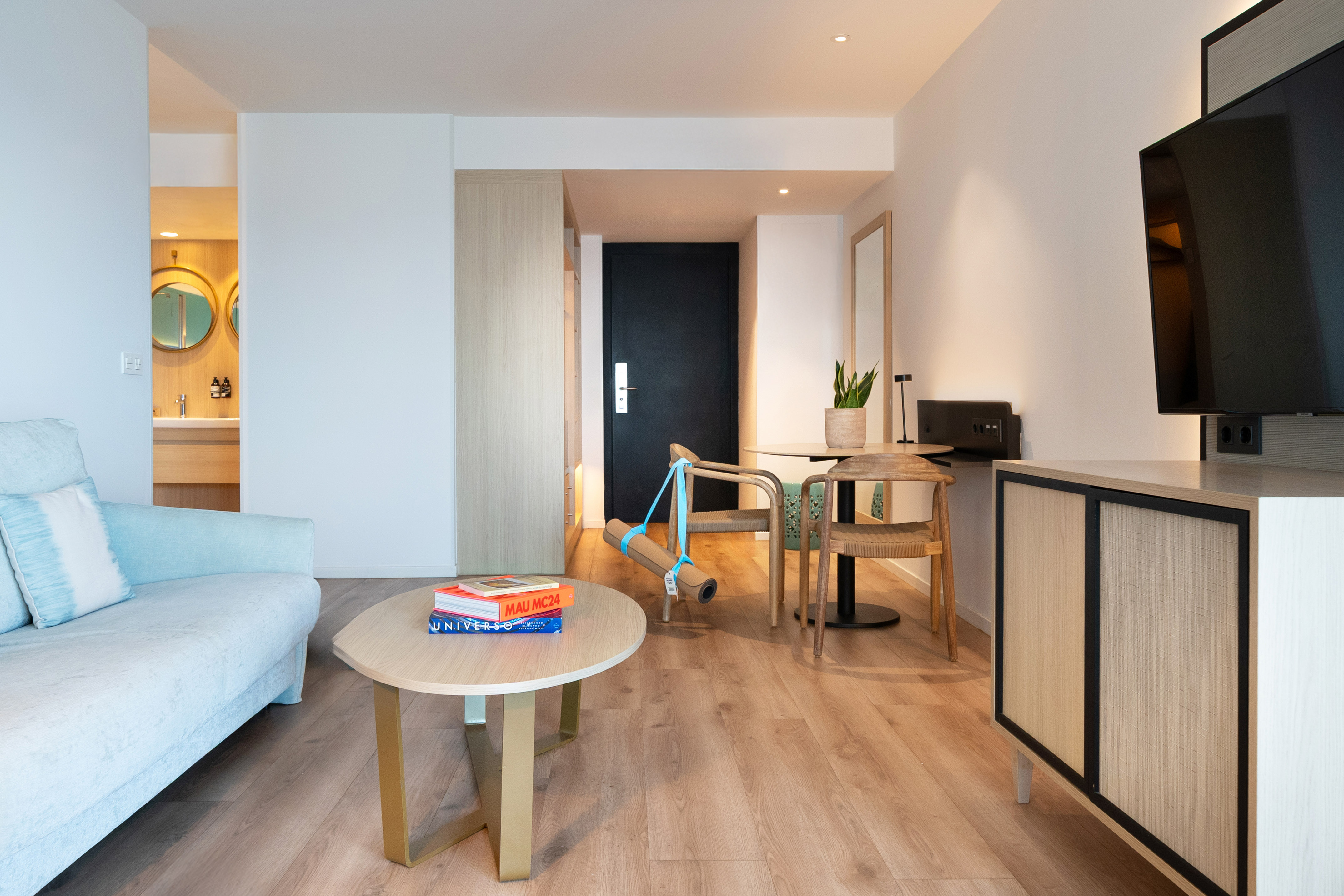 Stylish hotel suite living space: sofa, coffee table, yoga mat, wood accents.