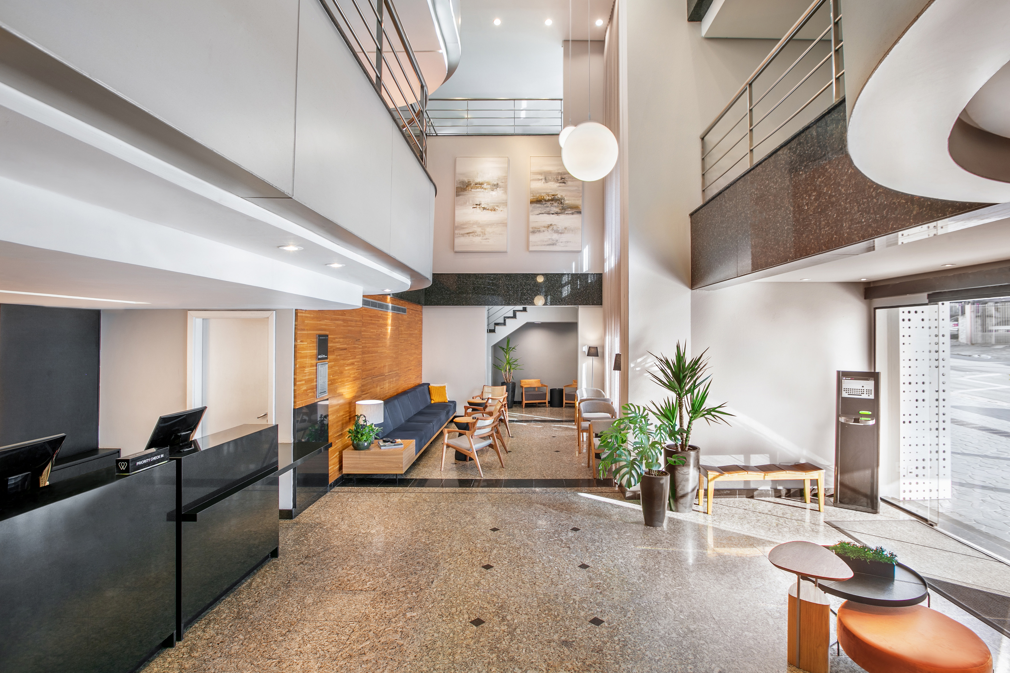Modern hotel lobby with black reception desk, lounge area, and tall plants.