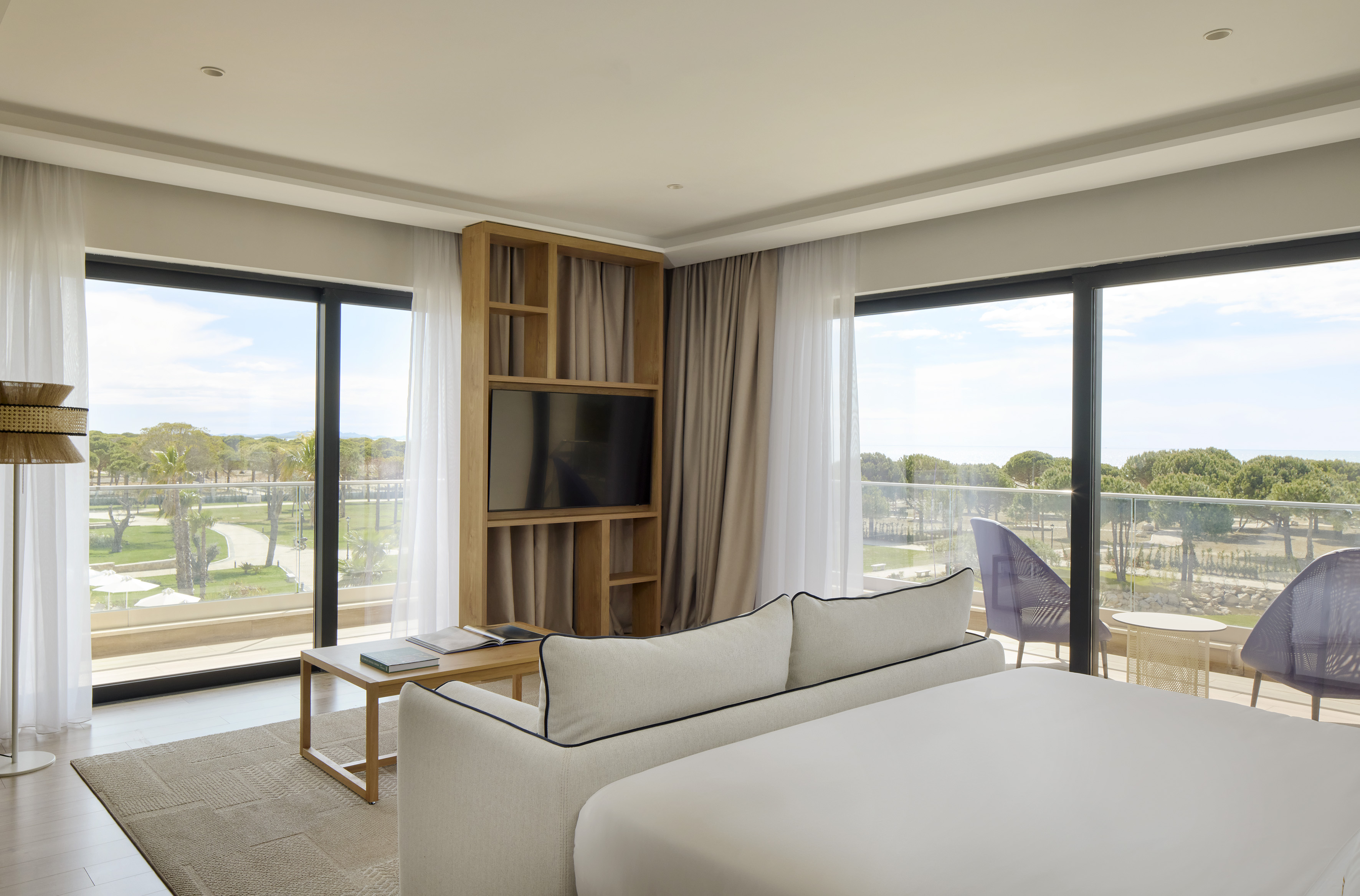 Spacious hotel room with bed, sofa, balcony, and resort garden ocean view.