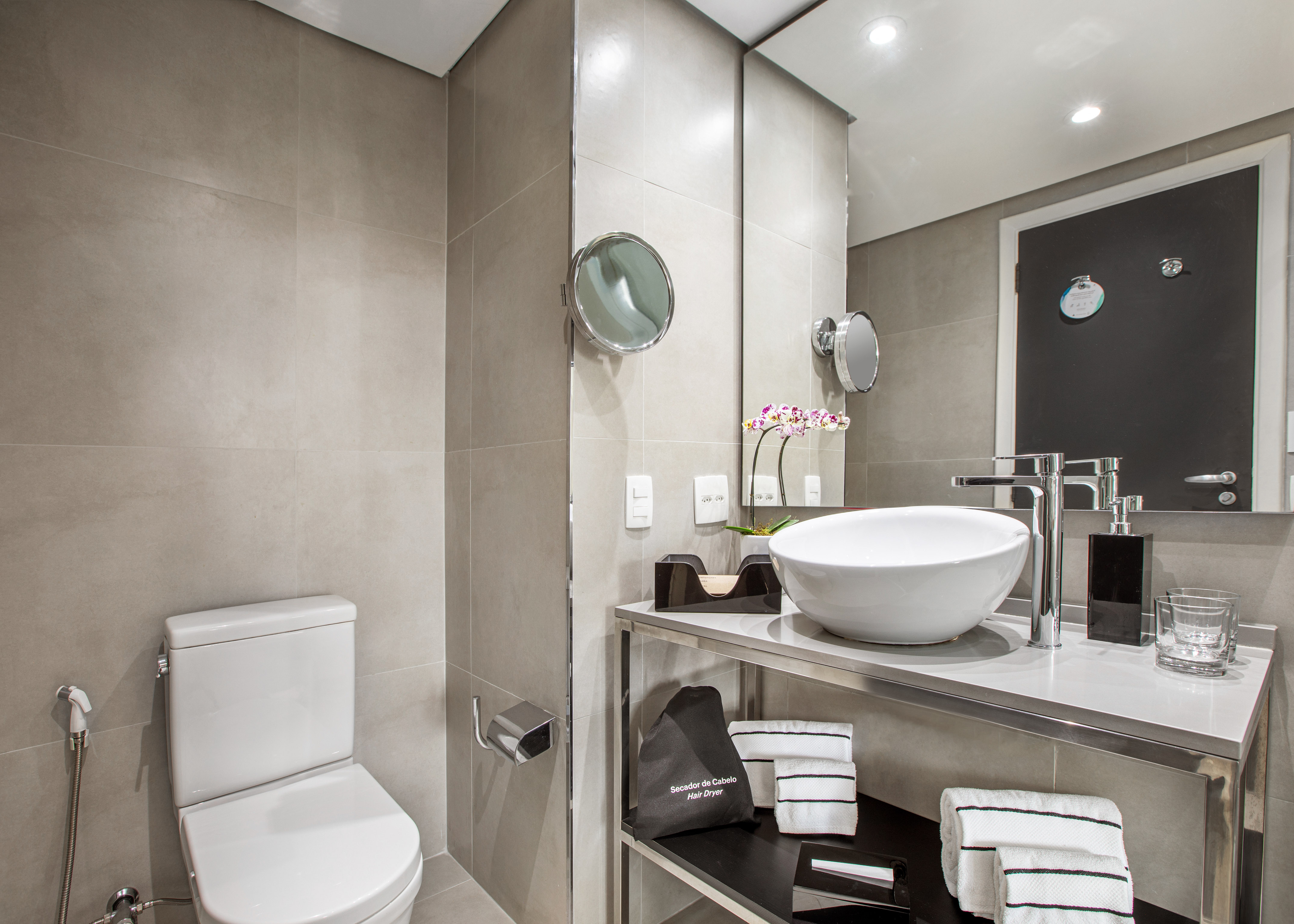 Modern hotel bathroom with gray tiles, white vessel sink vanity, and toilet.
