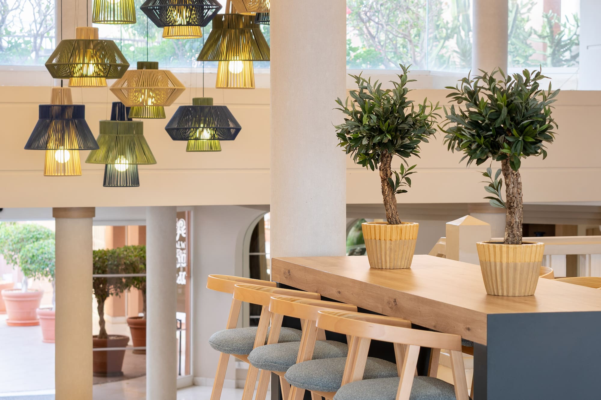 Stylish lobby bar with woven pendant lights, modern wooden stools, potted plants.