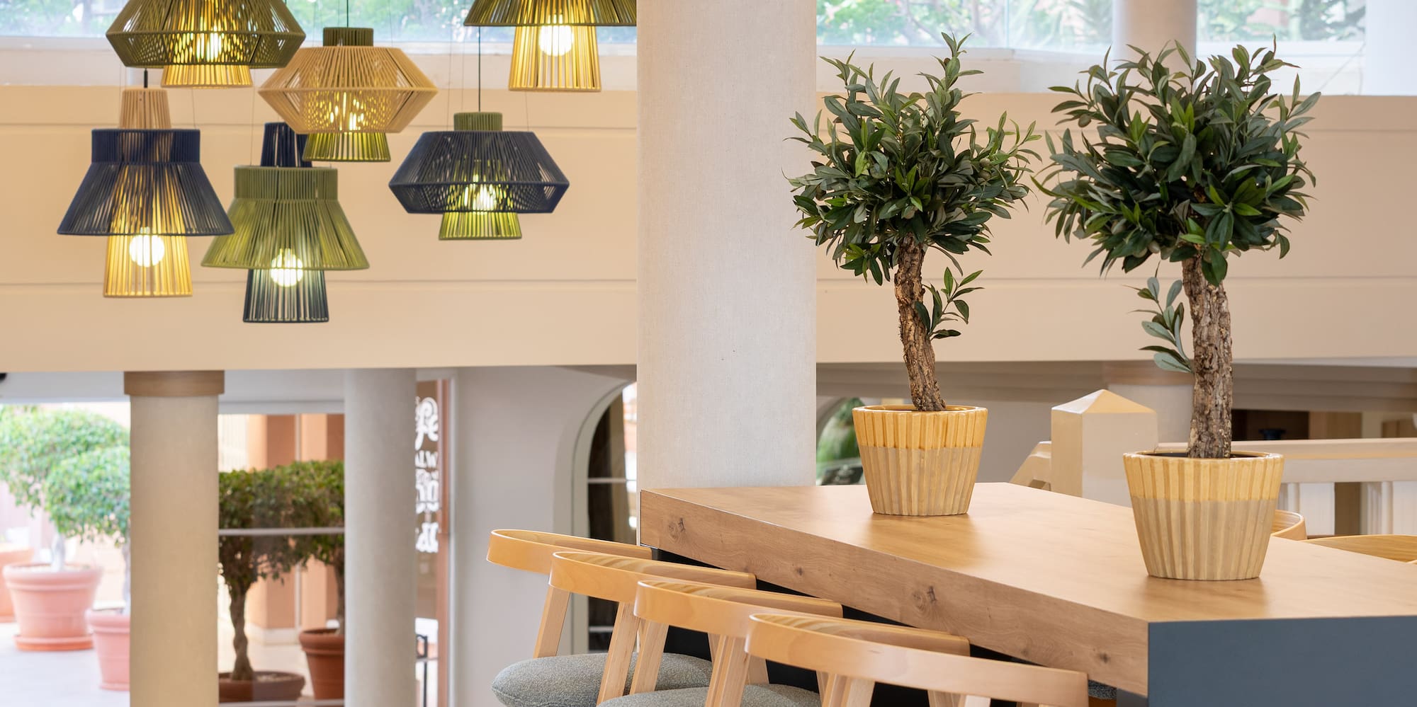 Stylish lobby bar with woven pendant lights, modern wooden stools, potted plants.