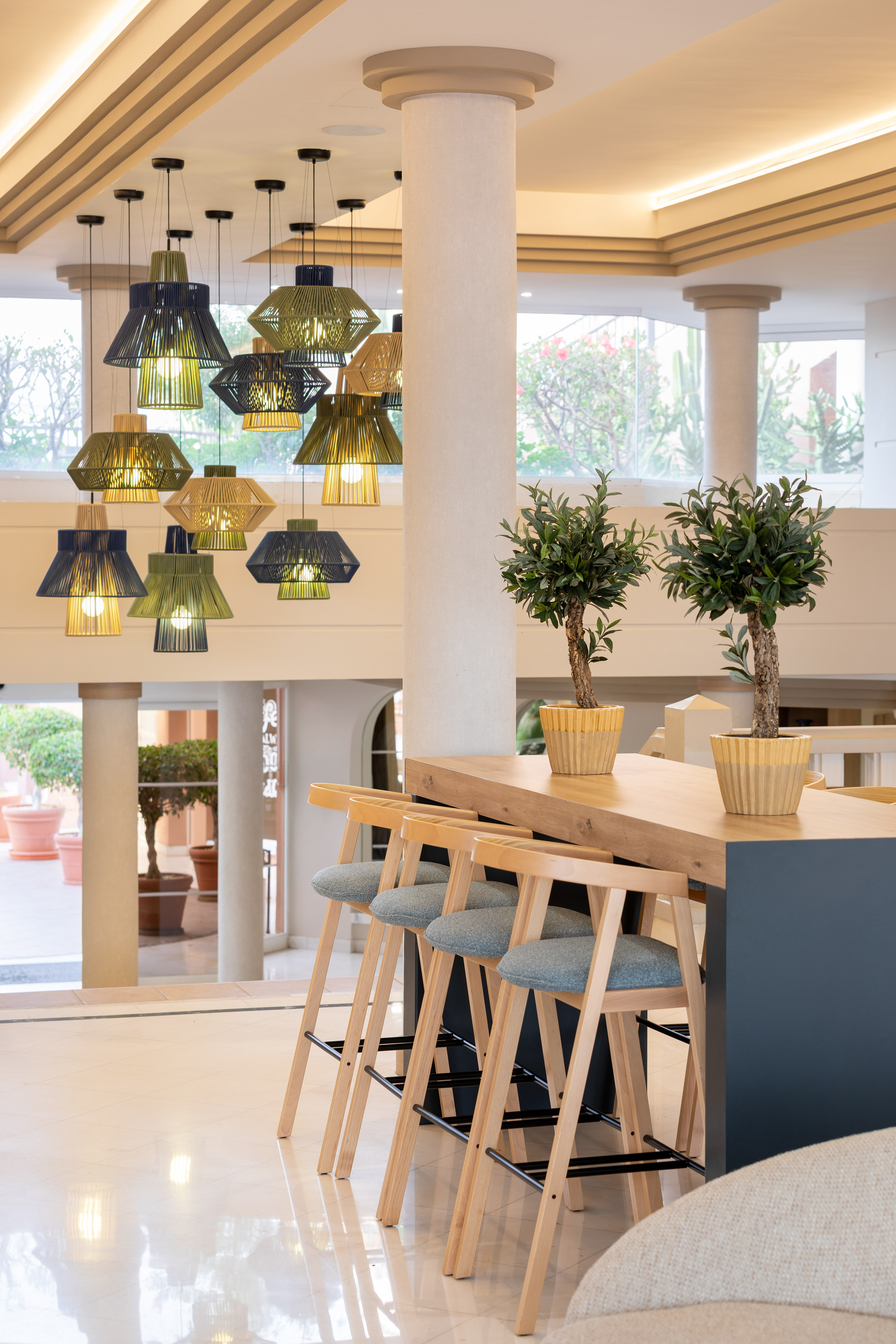 Stylish lobby bar with woven pendant lights, modern wooden stools, potted plants.