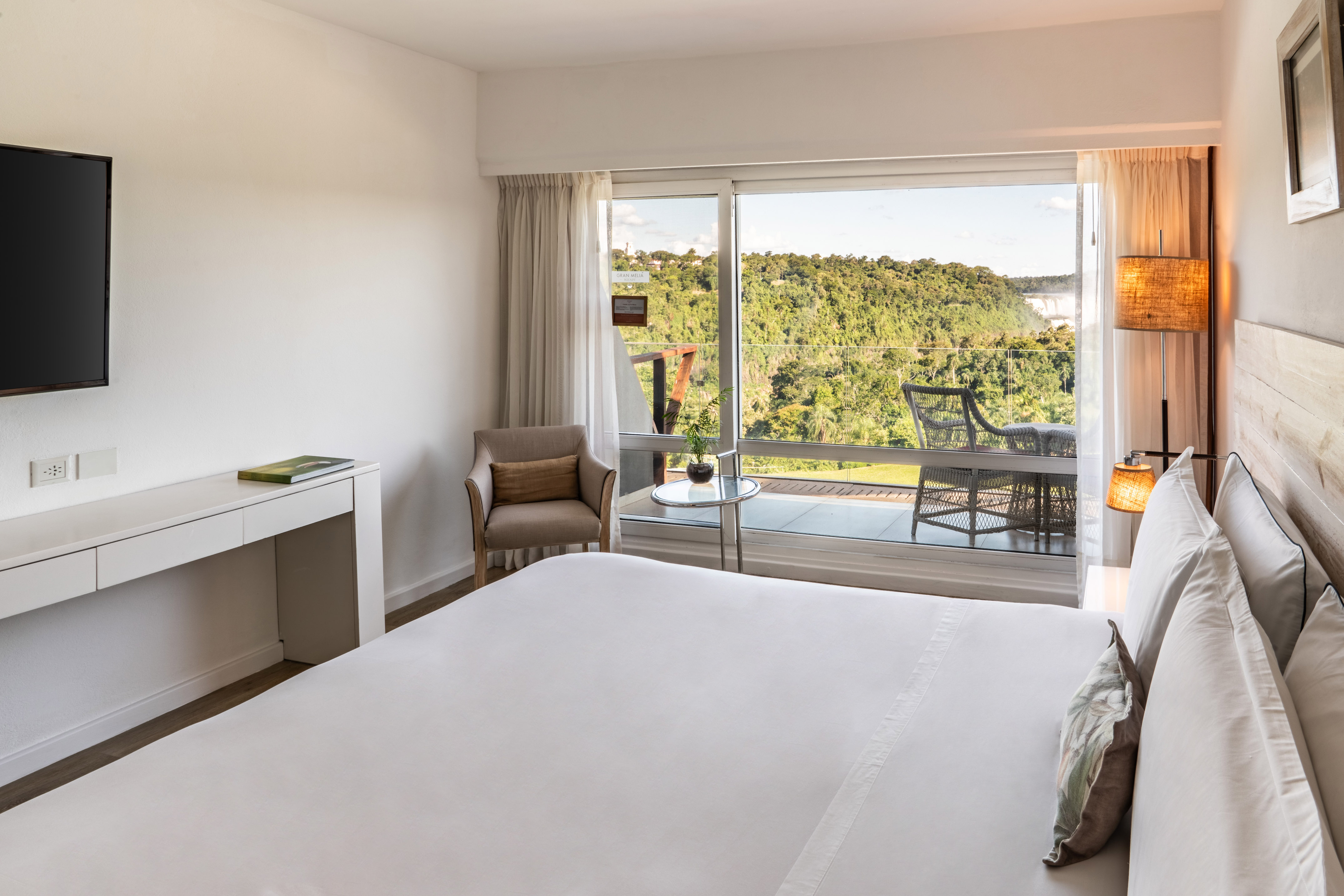 Modern hotel room with bed, balcony, and panoramic jungle view of Iguazu Falls.