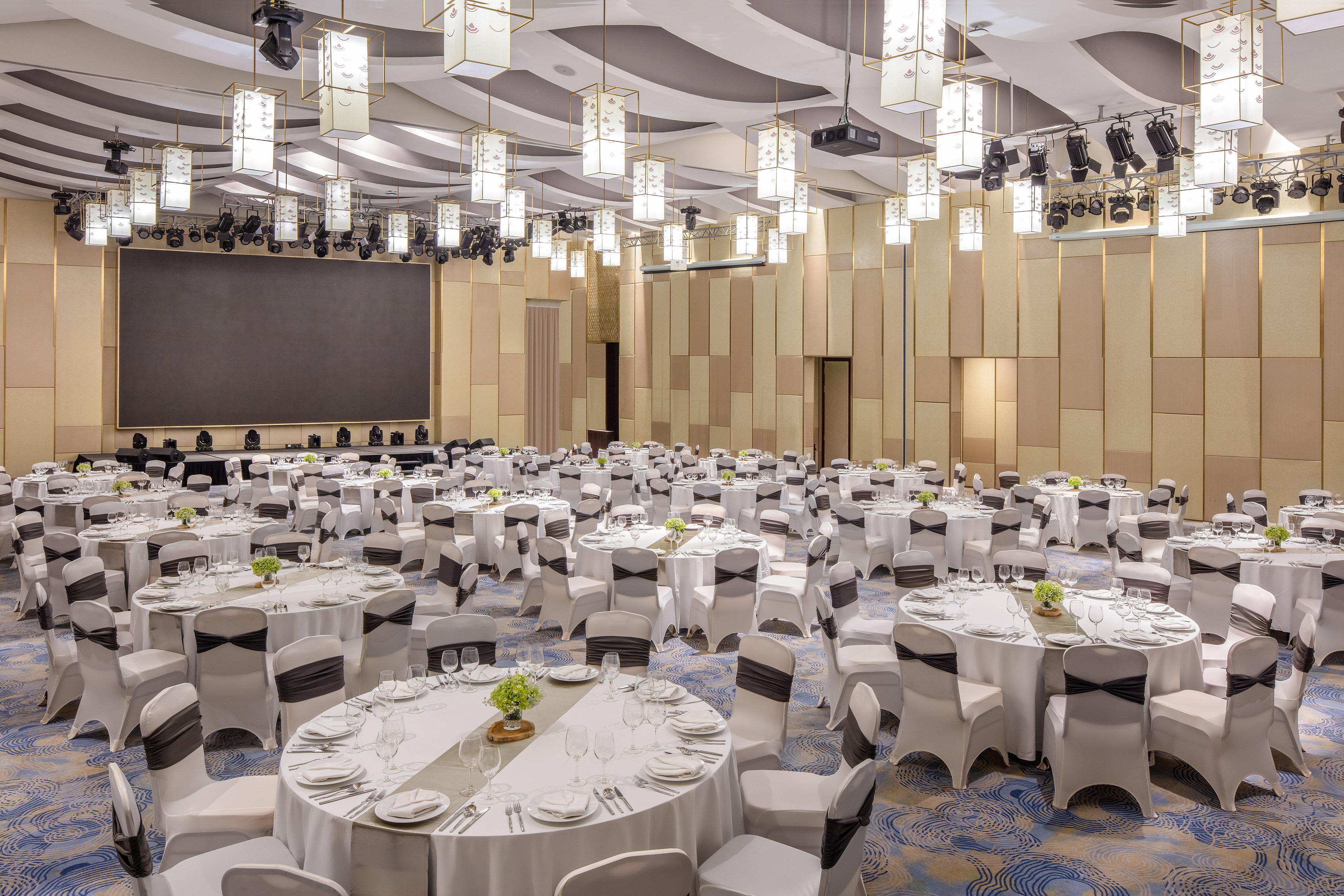 Elegant banquet hall with round tables, white chairs, and large event screen.