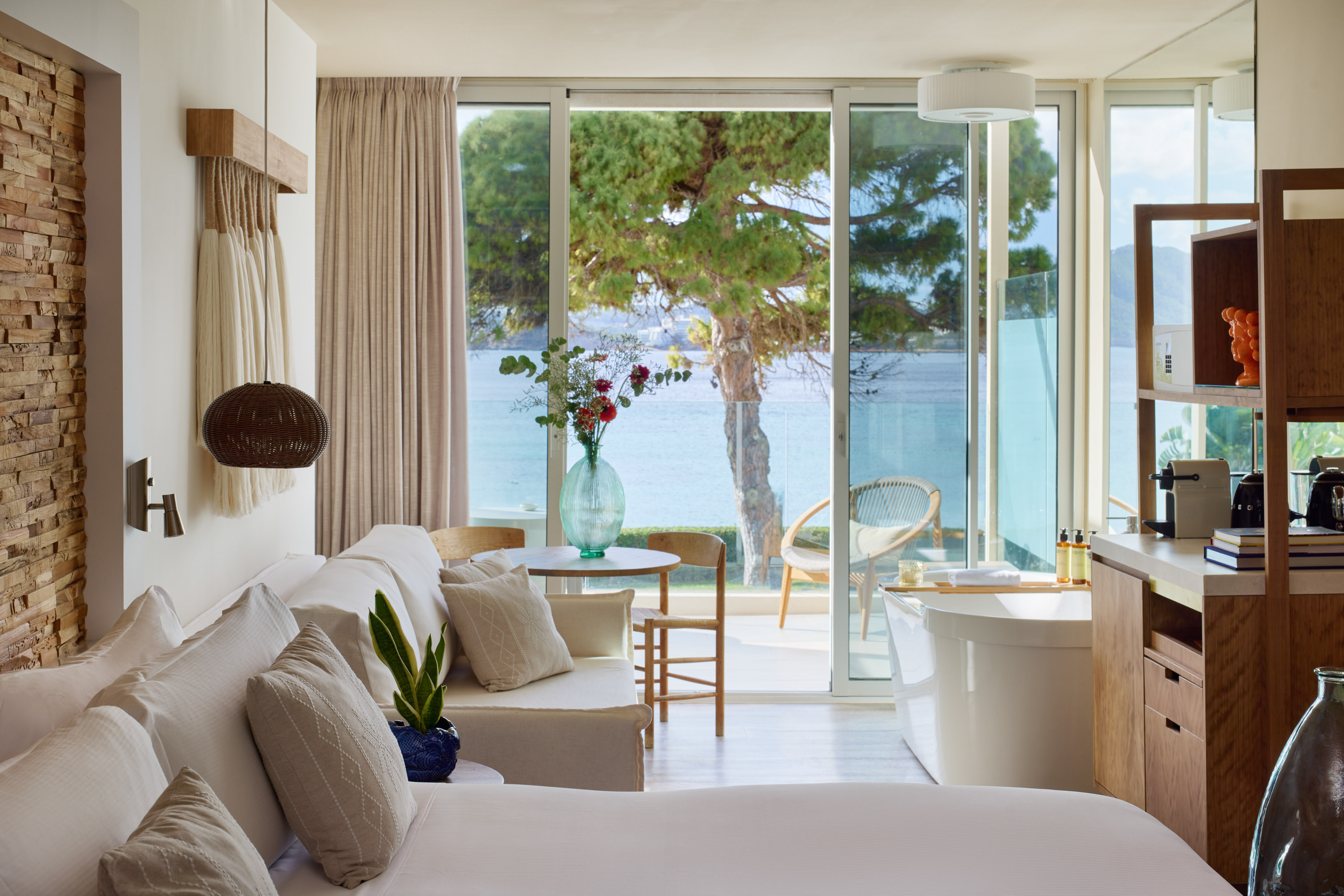 Modern hotel suite with ocean view, private balcony, king bed, and freestanding tub.
