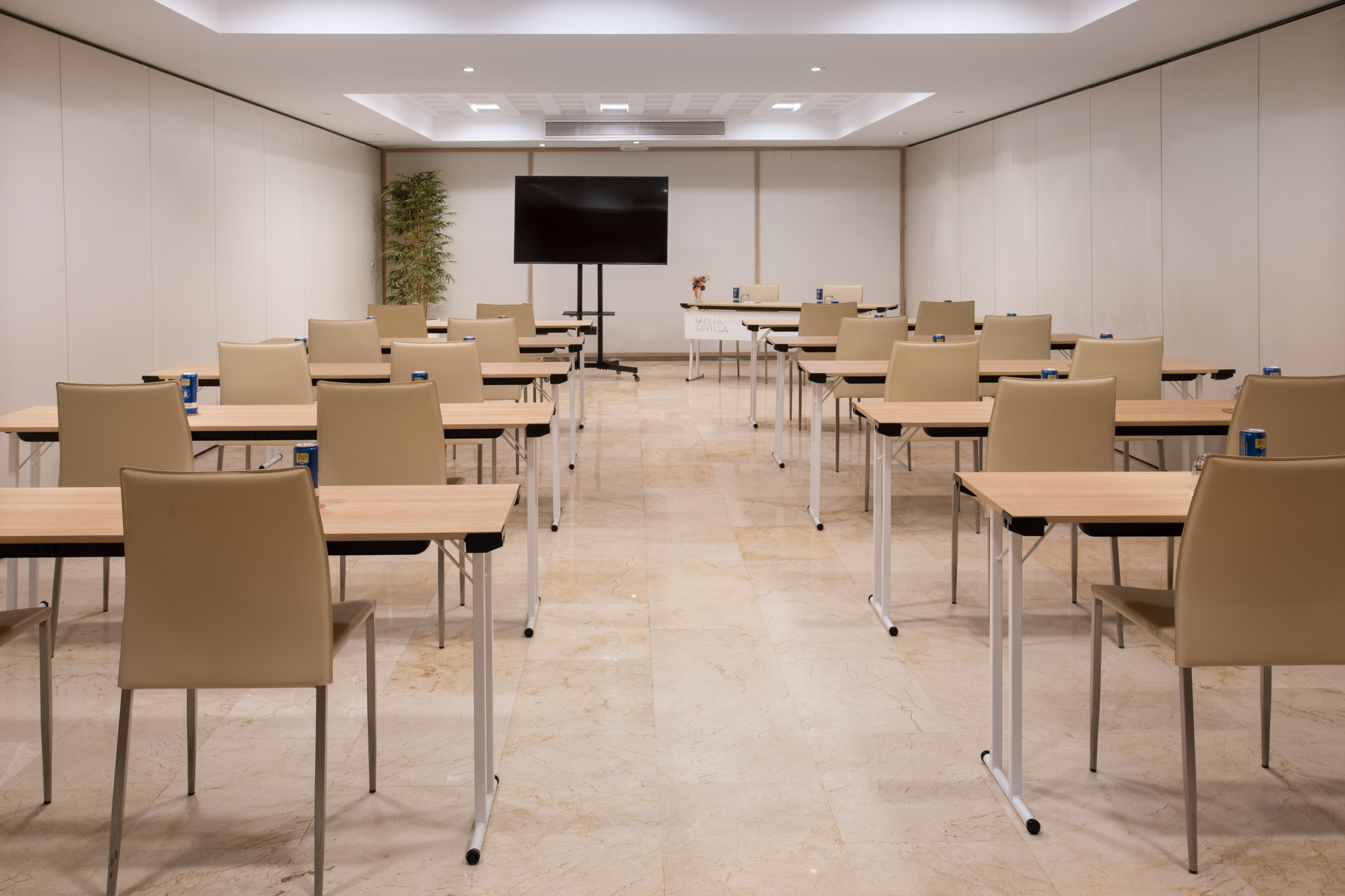 Meliá Sevilla meeting room with tables, beige chairs, and TV in classroom setup.