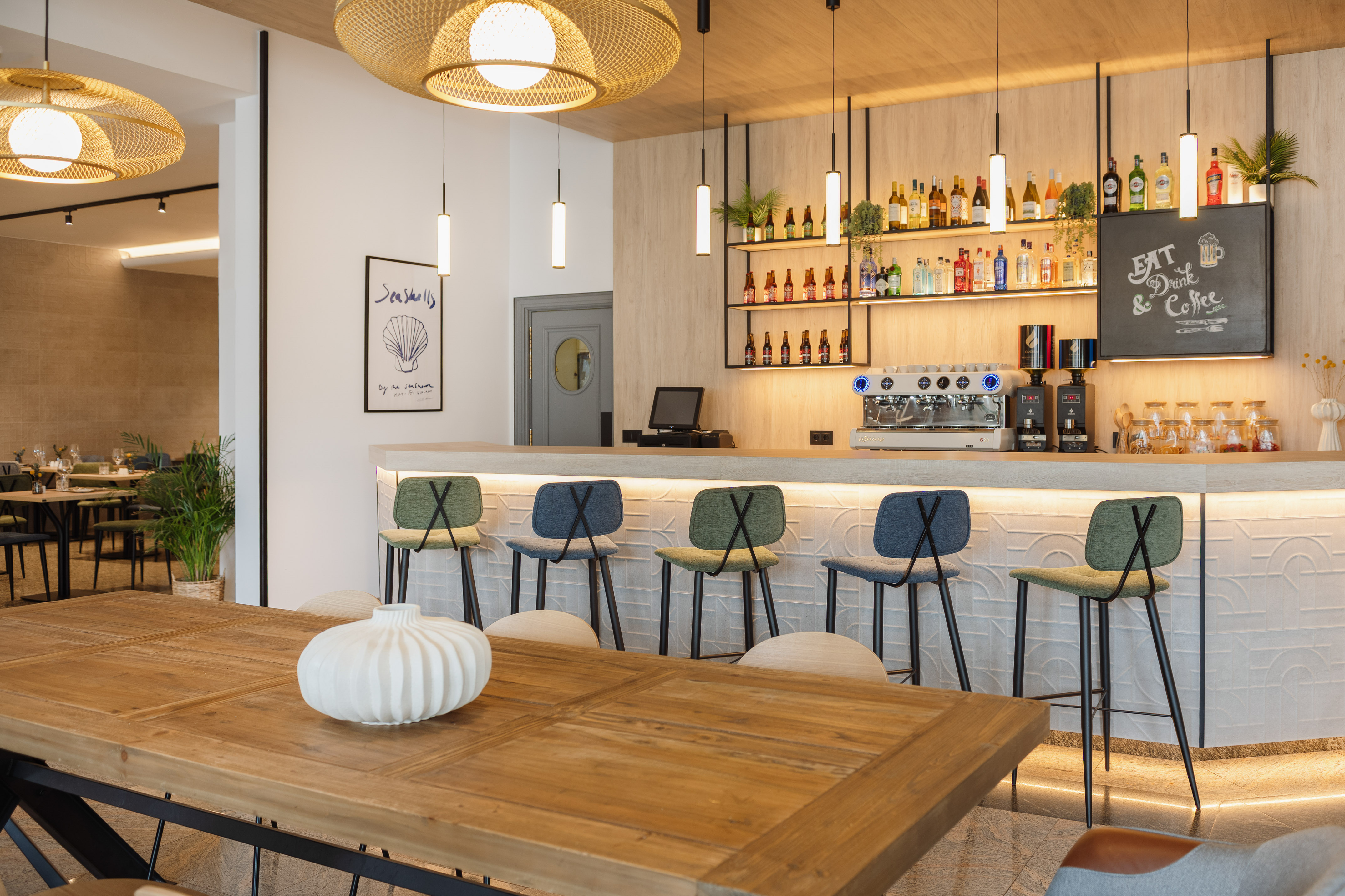 Modern bar interior with colorful stools, wooden table, and drinks display.