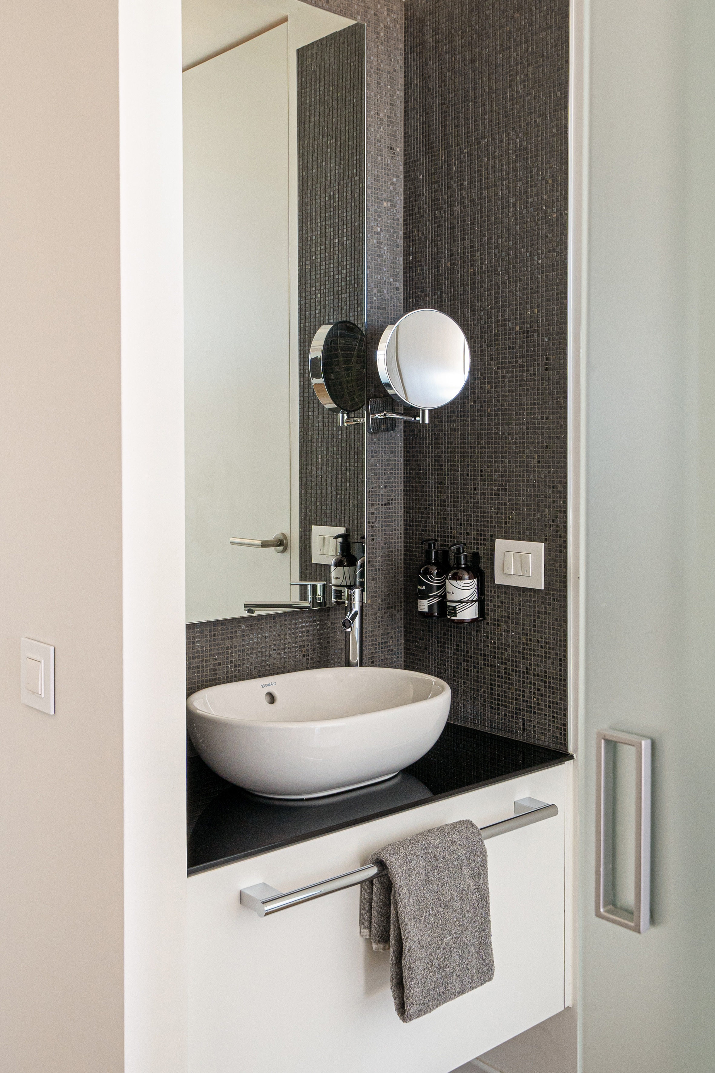 Modern bathroom: white vessel sink, dark mosaic tile, chrome faucet & mirror.
