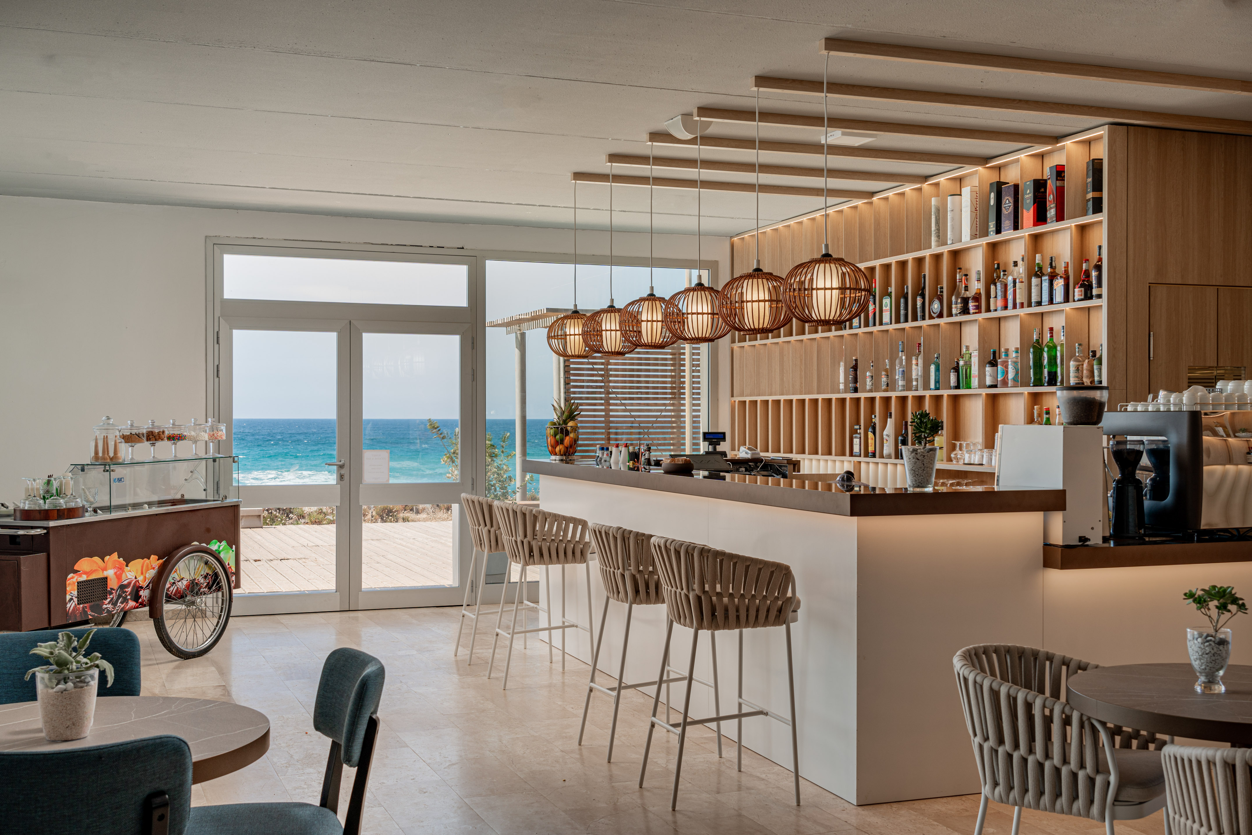 Modern beachfront bar interior with ocean view, wooden shelves, and bar stools.