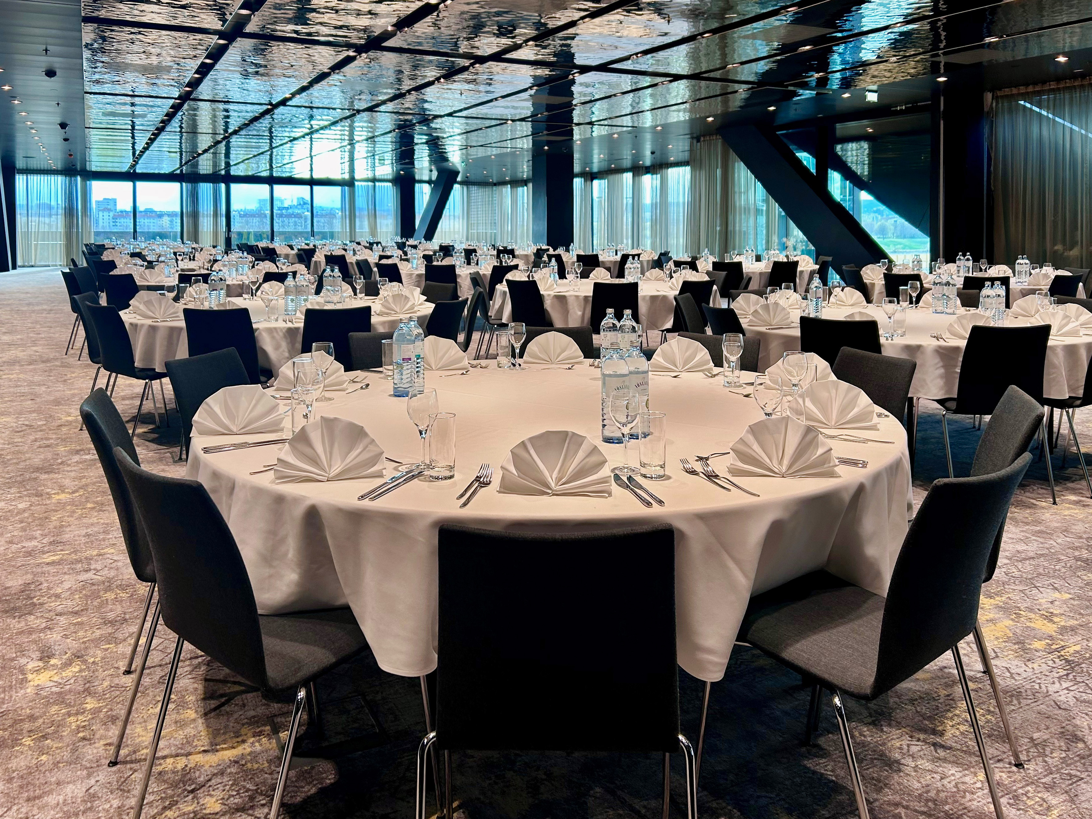 Large modern conference room with set round tables, dark chairs, and city view.