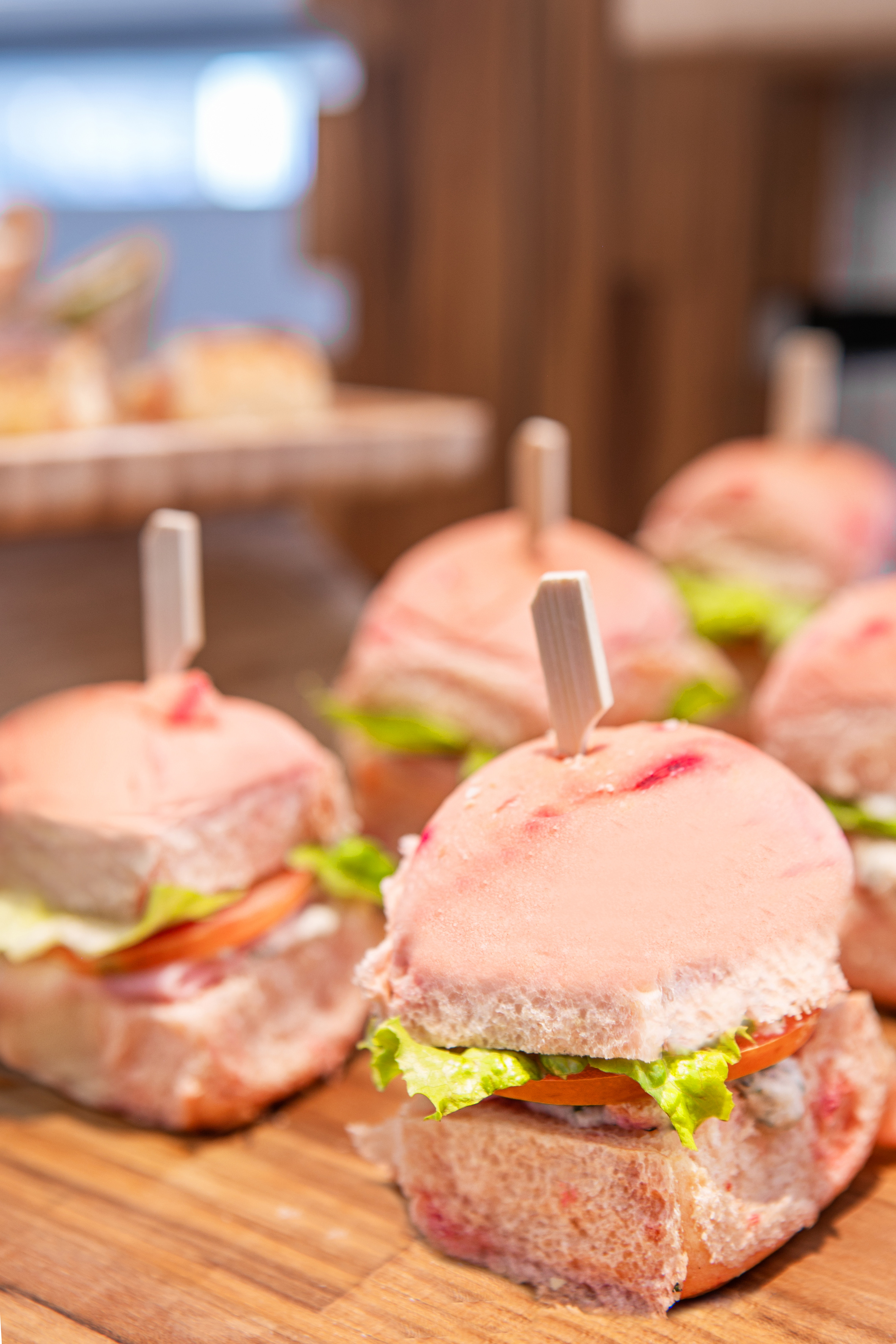 Buffet table with pink bun mini-burgers, lettuce, and tomato.