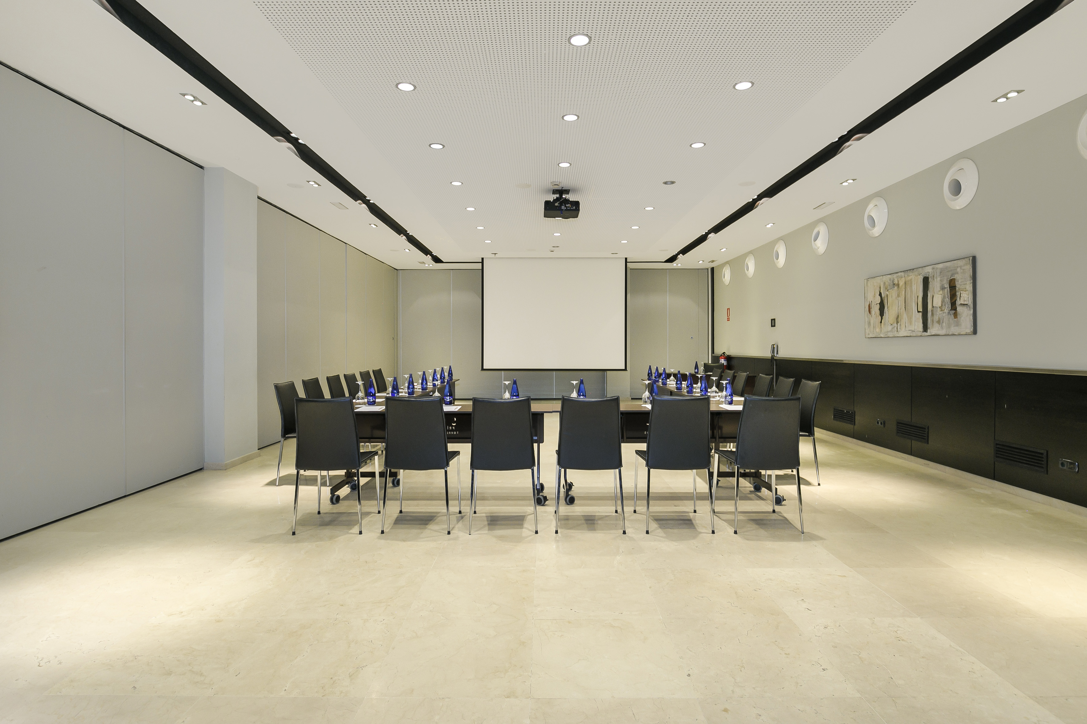 Professional conference room with U-shaped table, chairs, and projector screen.