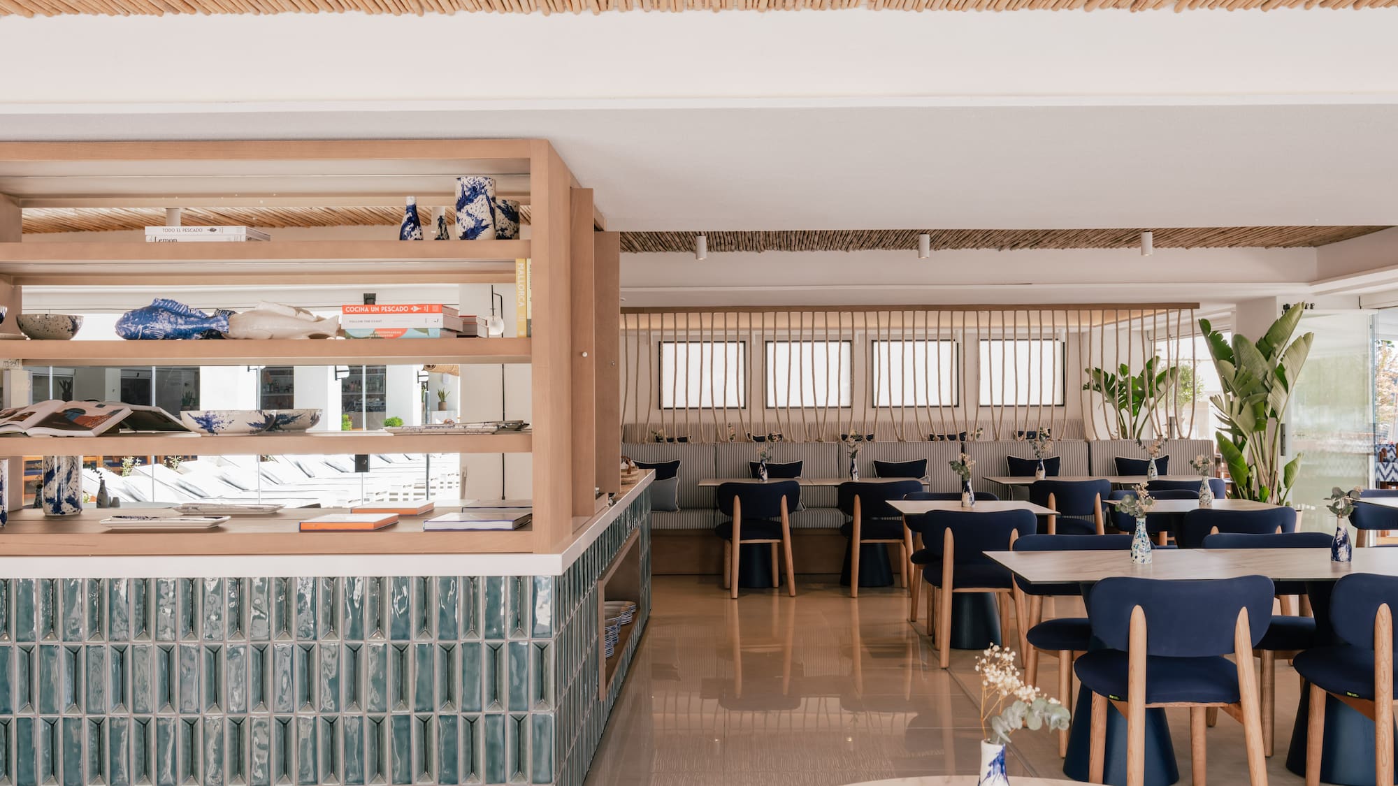 Coastal restaurant with bamboo ceiling, blue chairs, and teal counter.