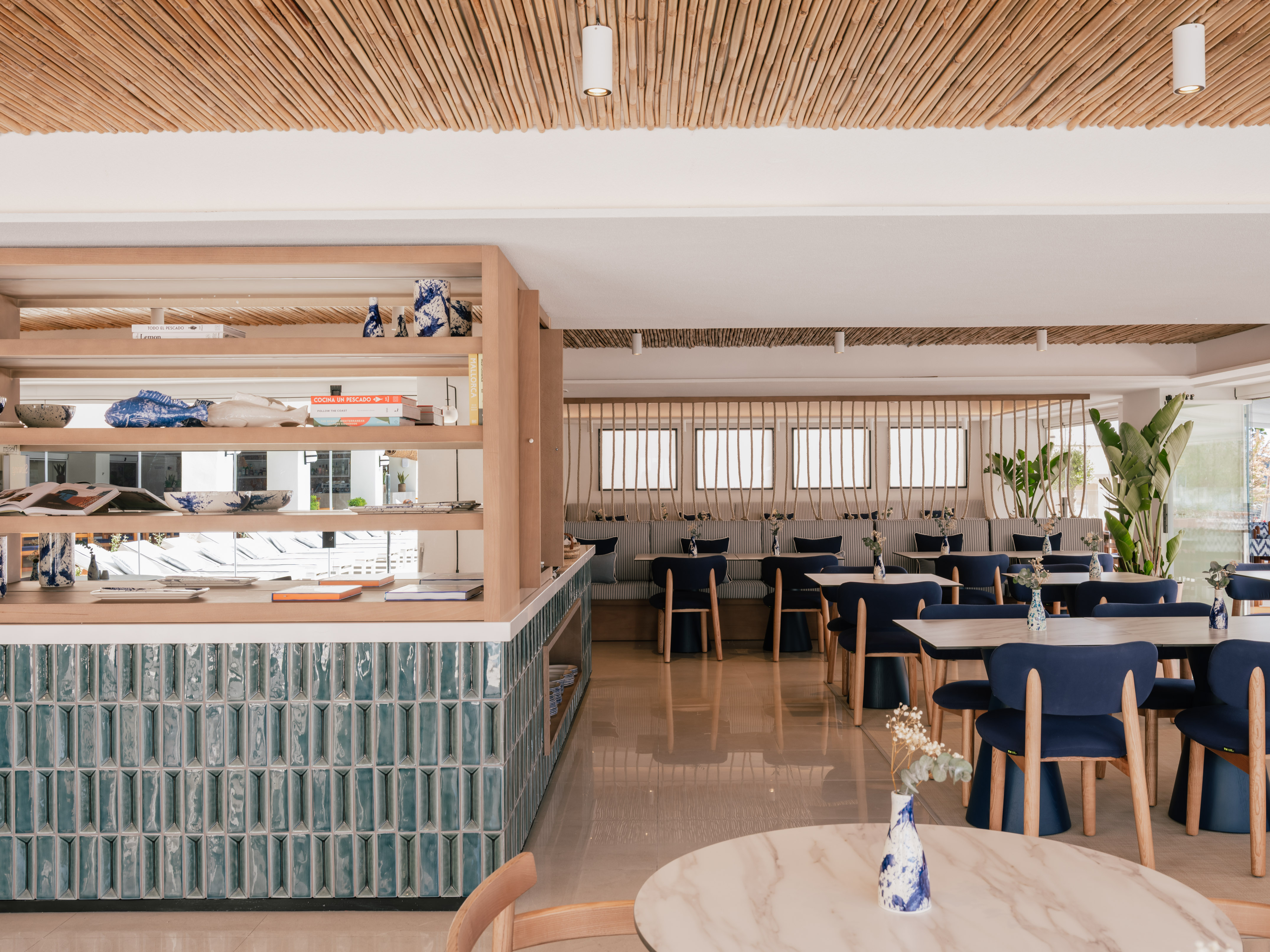 Coastal restaurant with bamboo ceiling, blue chairs, and teal counter.