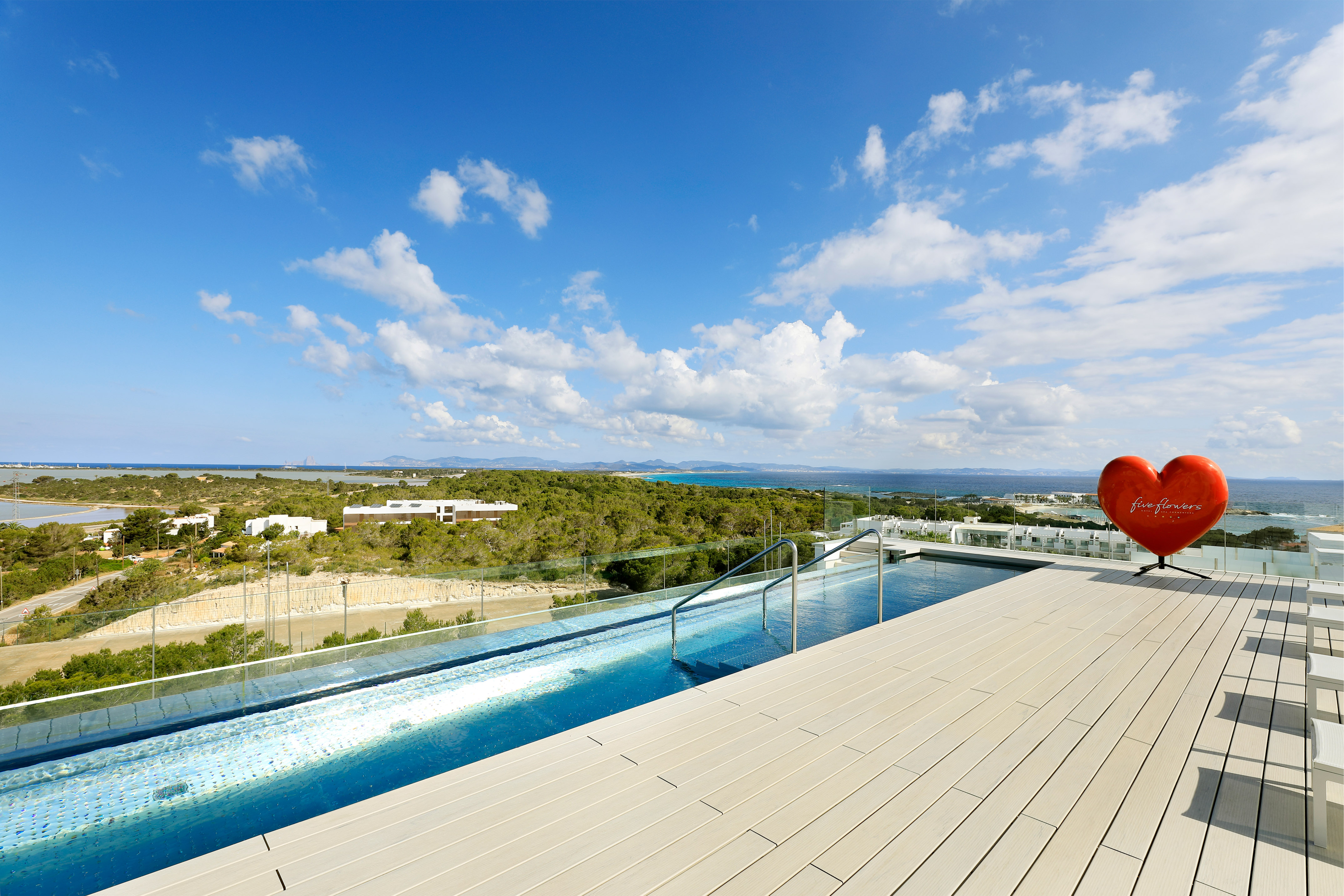 Rooftop infinity pool with wooden deck, ocean view, and a red heart sculpture.