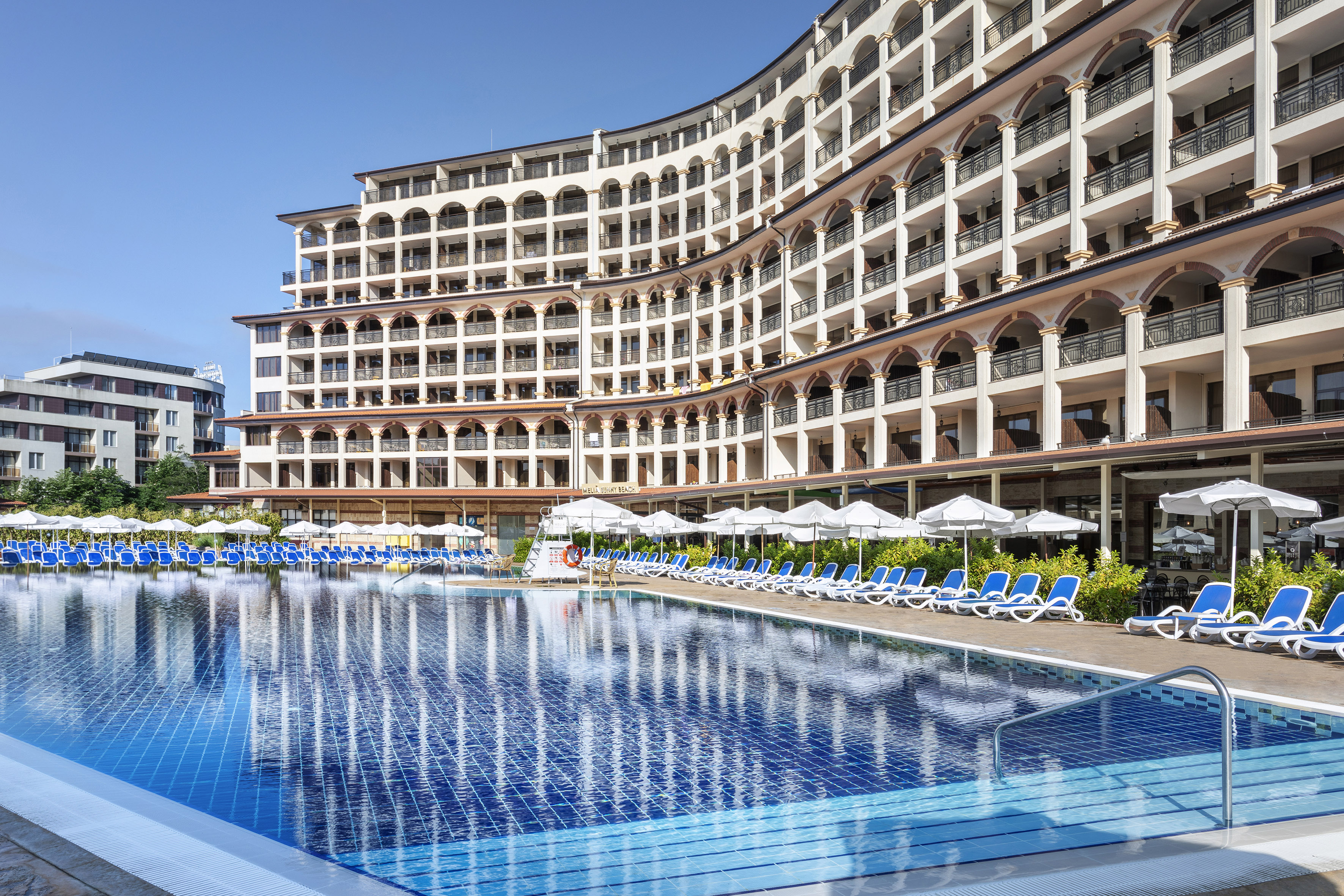 ein Pool mit Sonnenschirmen und Sonnenliegen vor einem Gebäude