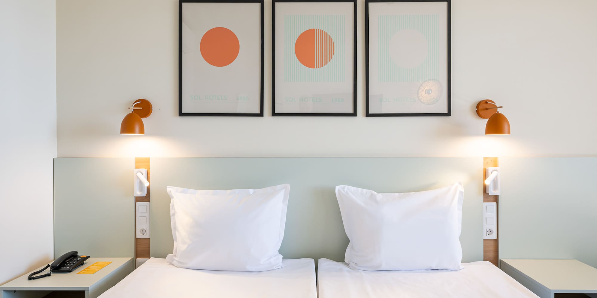 Sol Hotels twin bedroom with white beds, modern art, and orange wall lamps.