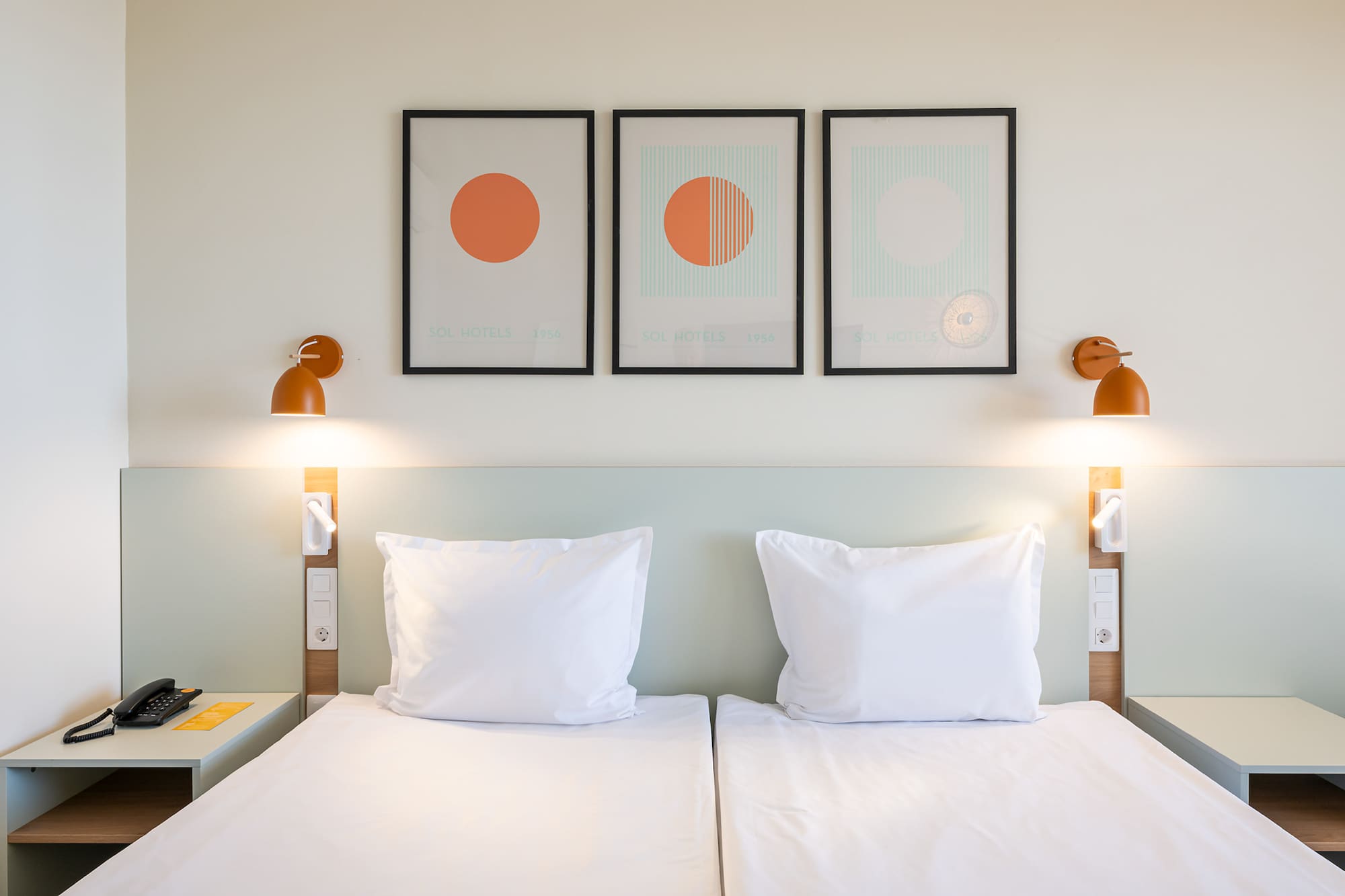 Sol Hotels twin bedroom with white beds, modern art, and orange wall lamps.