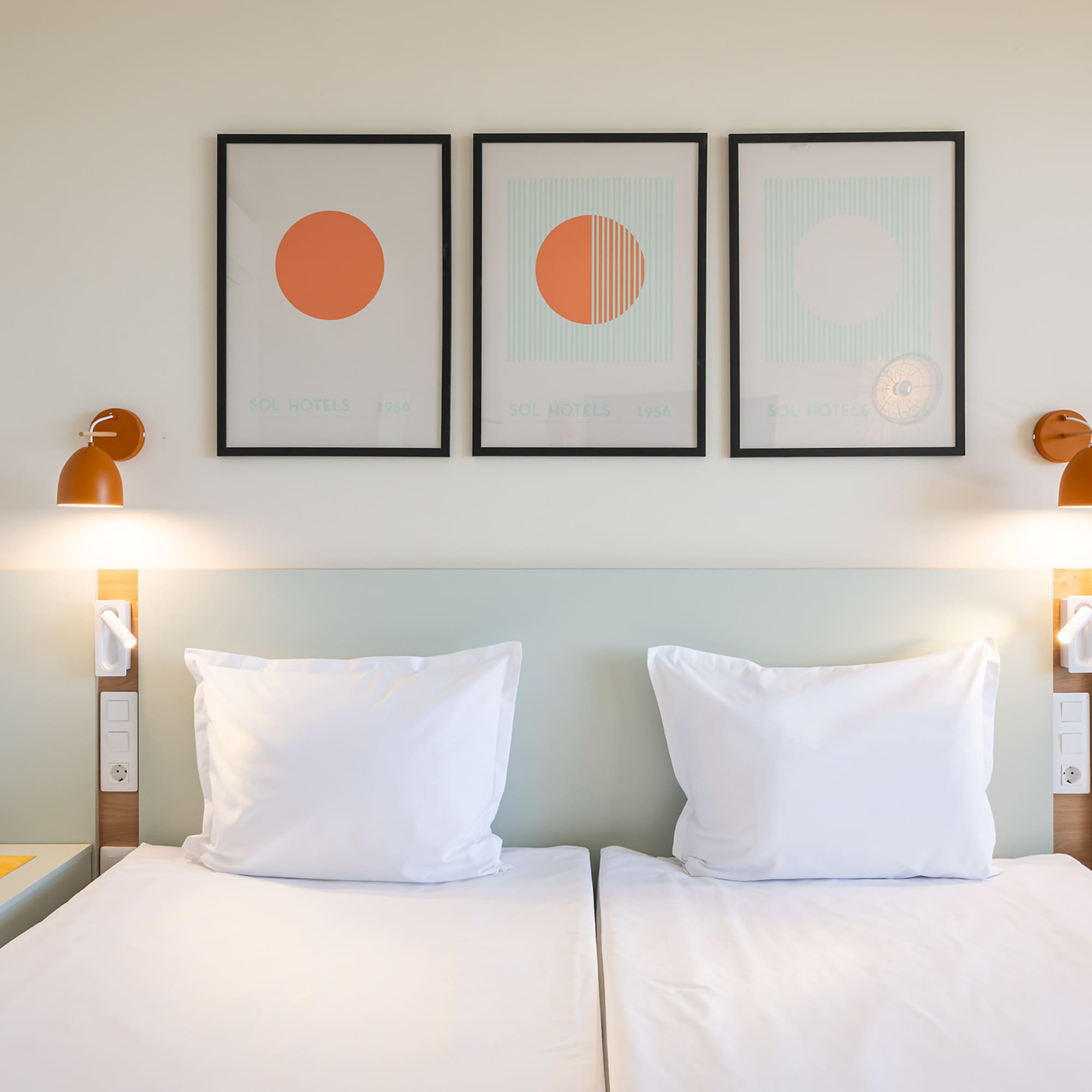 Sol Hotels twin bedroom with white beds, modern art, and orange wall lamps.