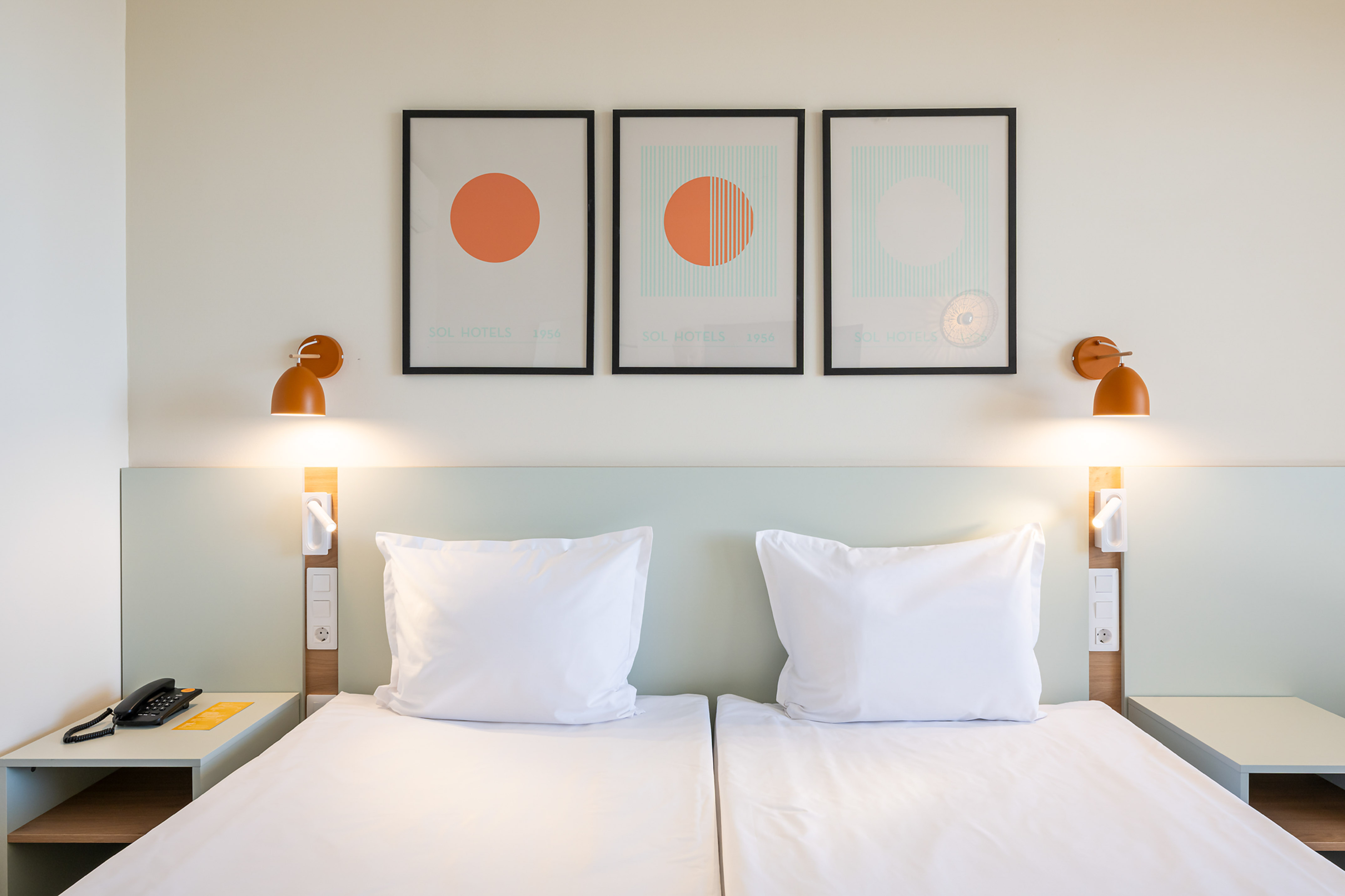 Sol Hotels twin bedroom with white beds, modern art, and orange wall lamps.
