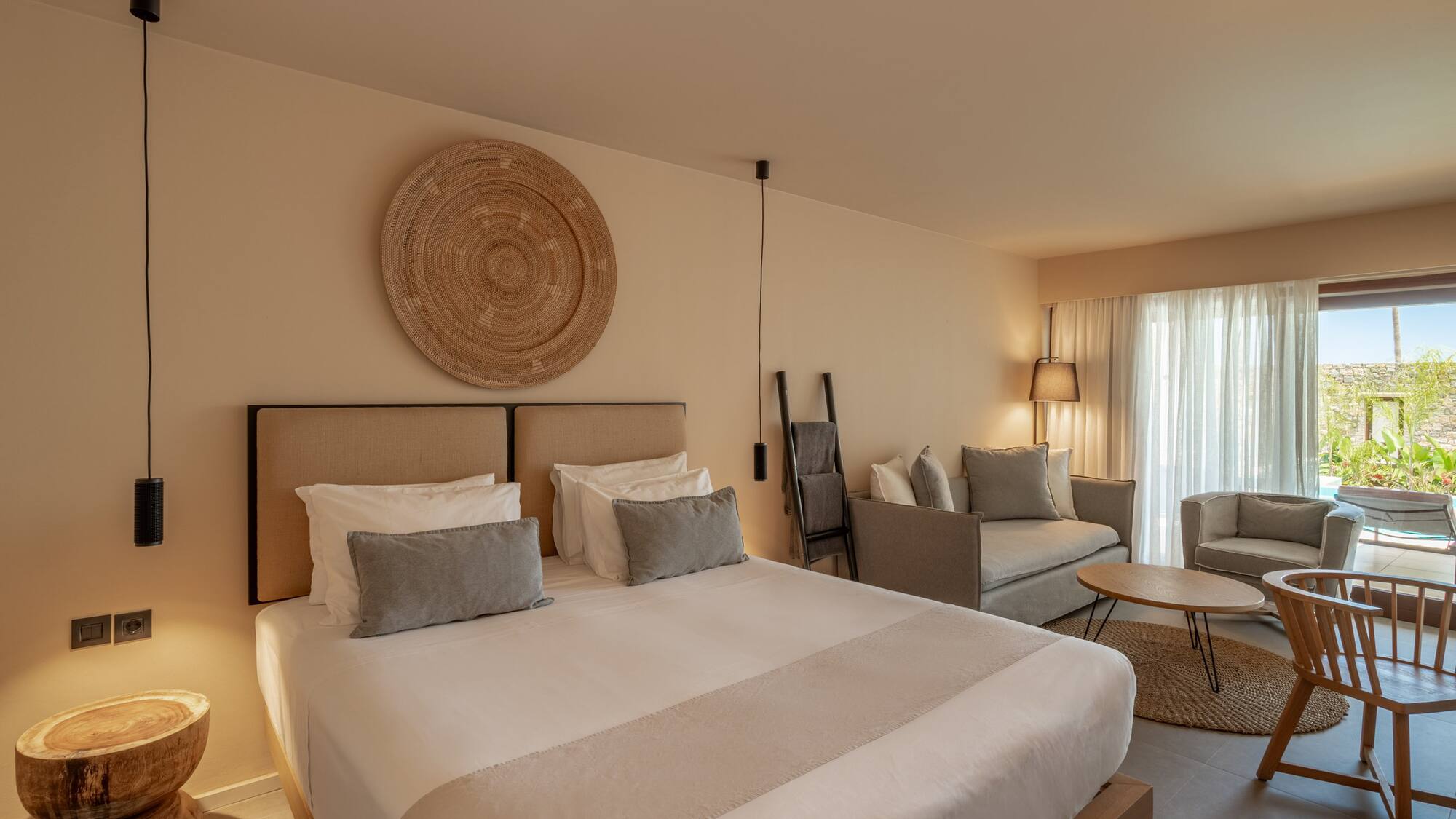 Neutral modern hotel suite with bed, woven wall decor, and a living area.