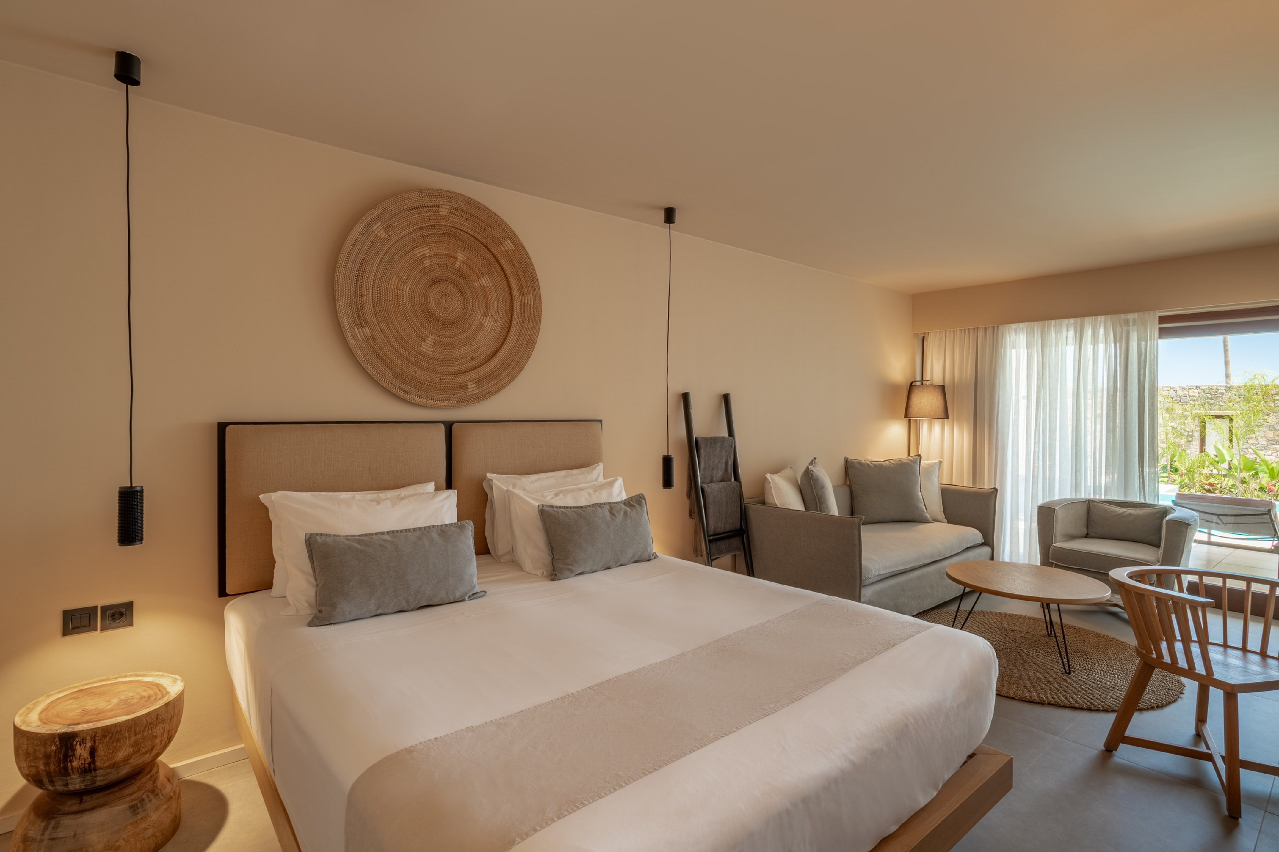 Neutral modern hotel suite with bed, woven wall decor, and a living area.