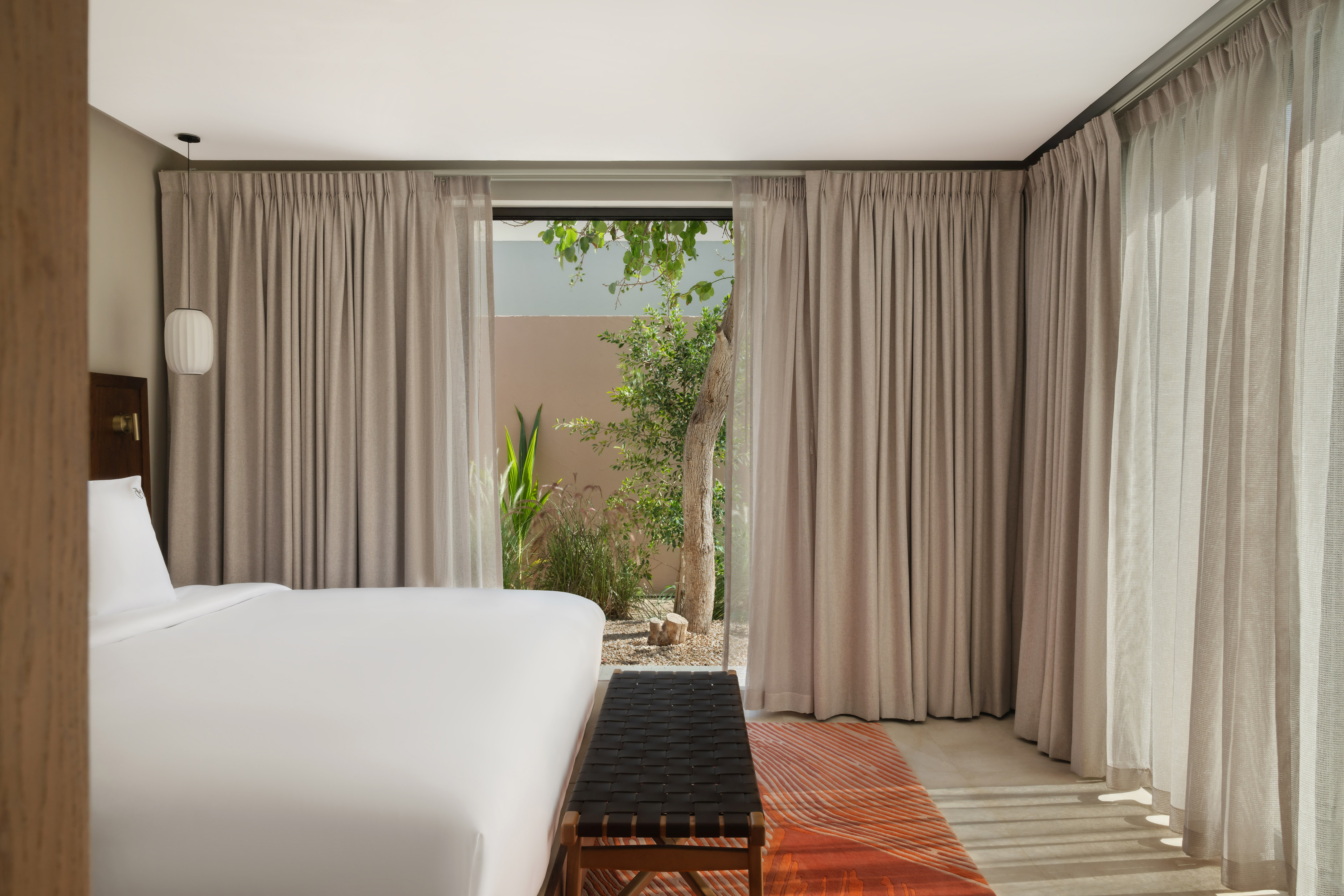 Modern hotel bedroom with white bed, black bench, and private garden view.
