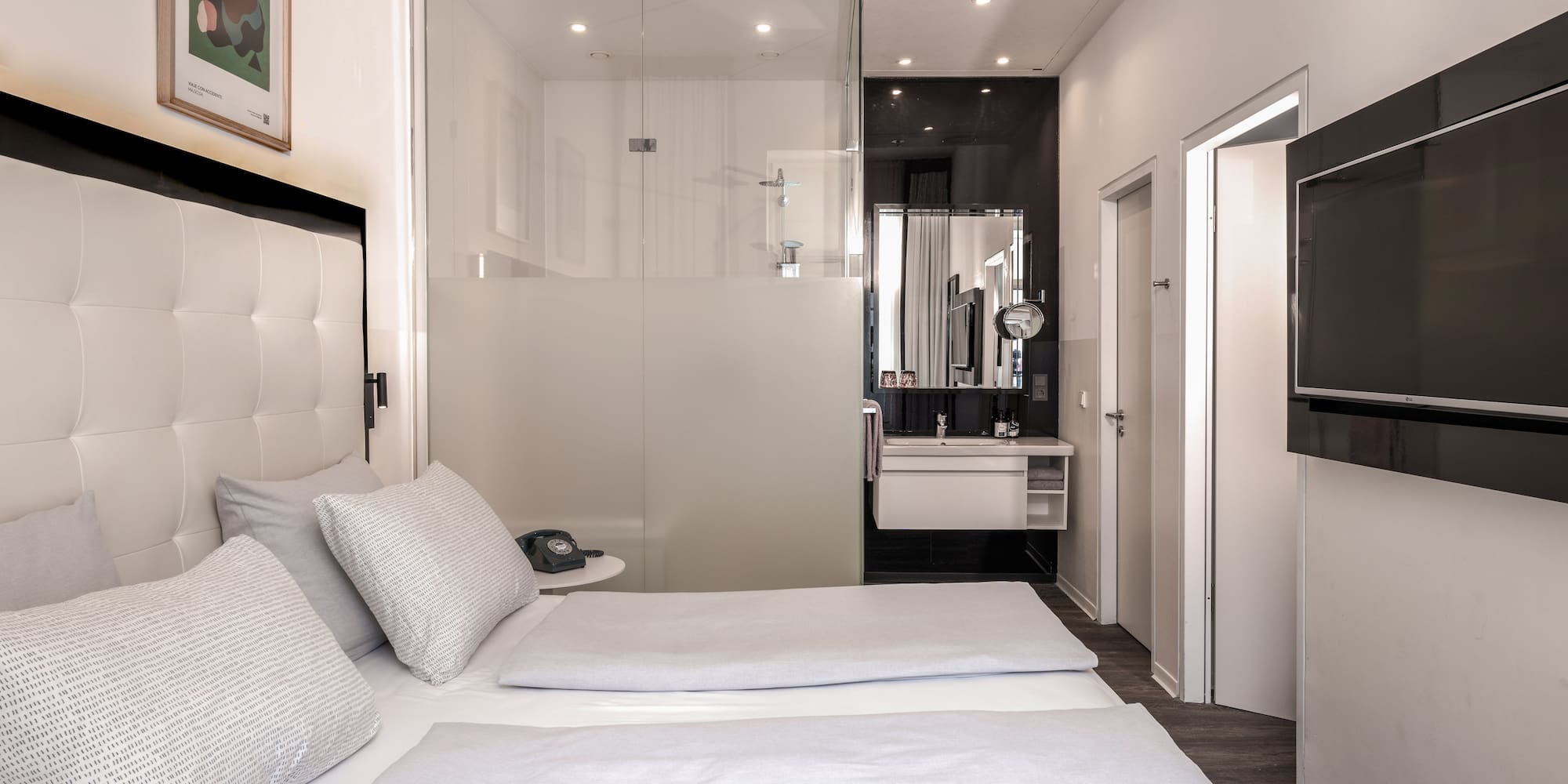 Modern hotel room with twin beds, glass bathroom, and wall-mounted TV.