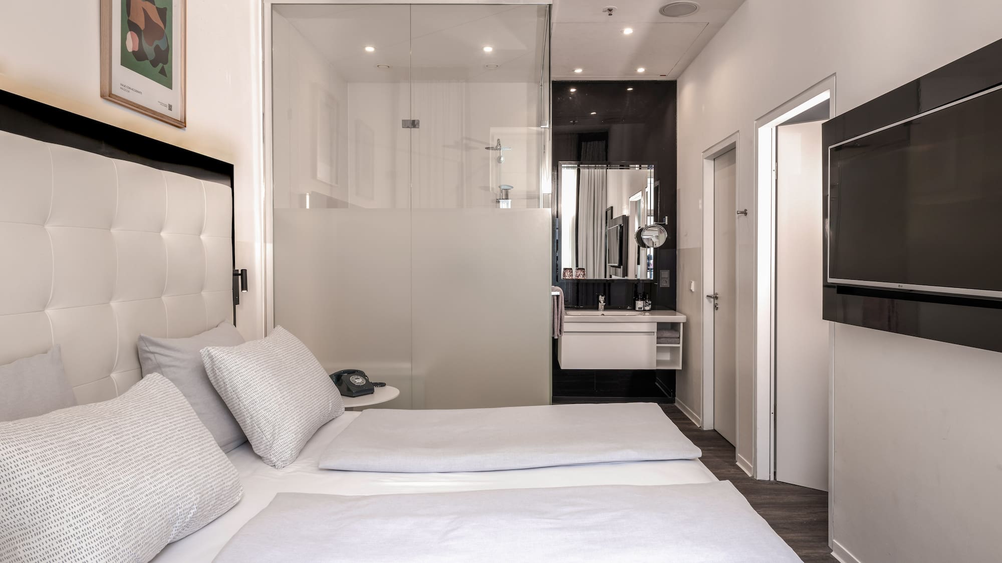 Modern hotel room with twin beds, glass bathroom, and wall-mounted TV.