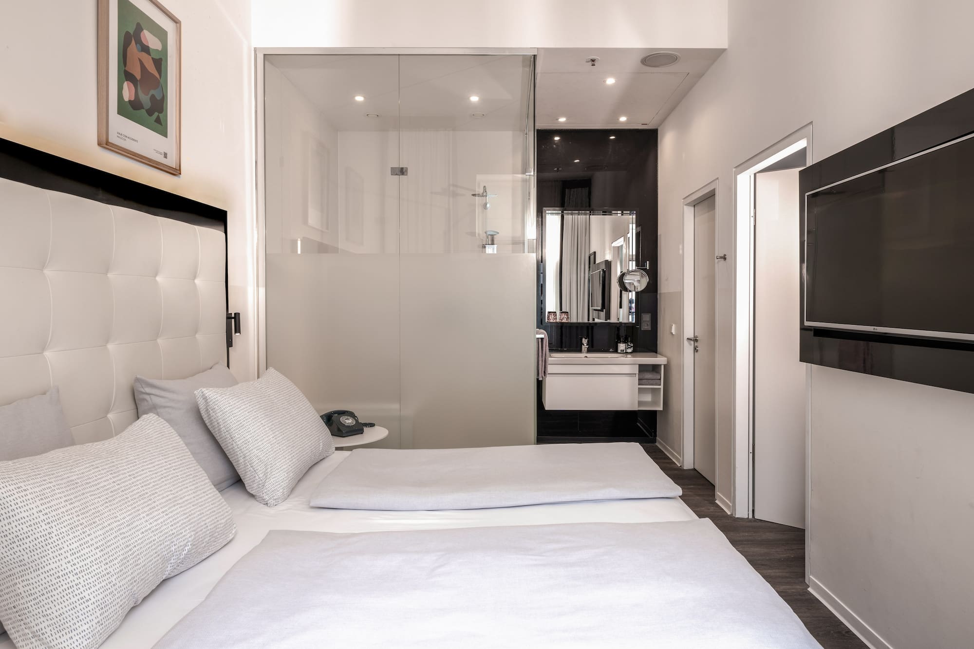 Modern hotel room with twin beds, glass bathroom, and wall-mounted TV.