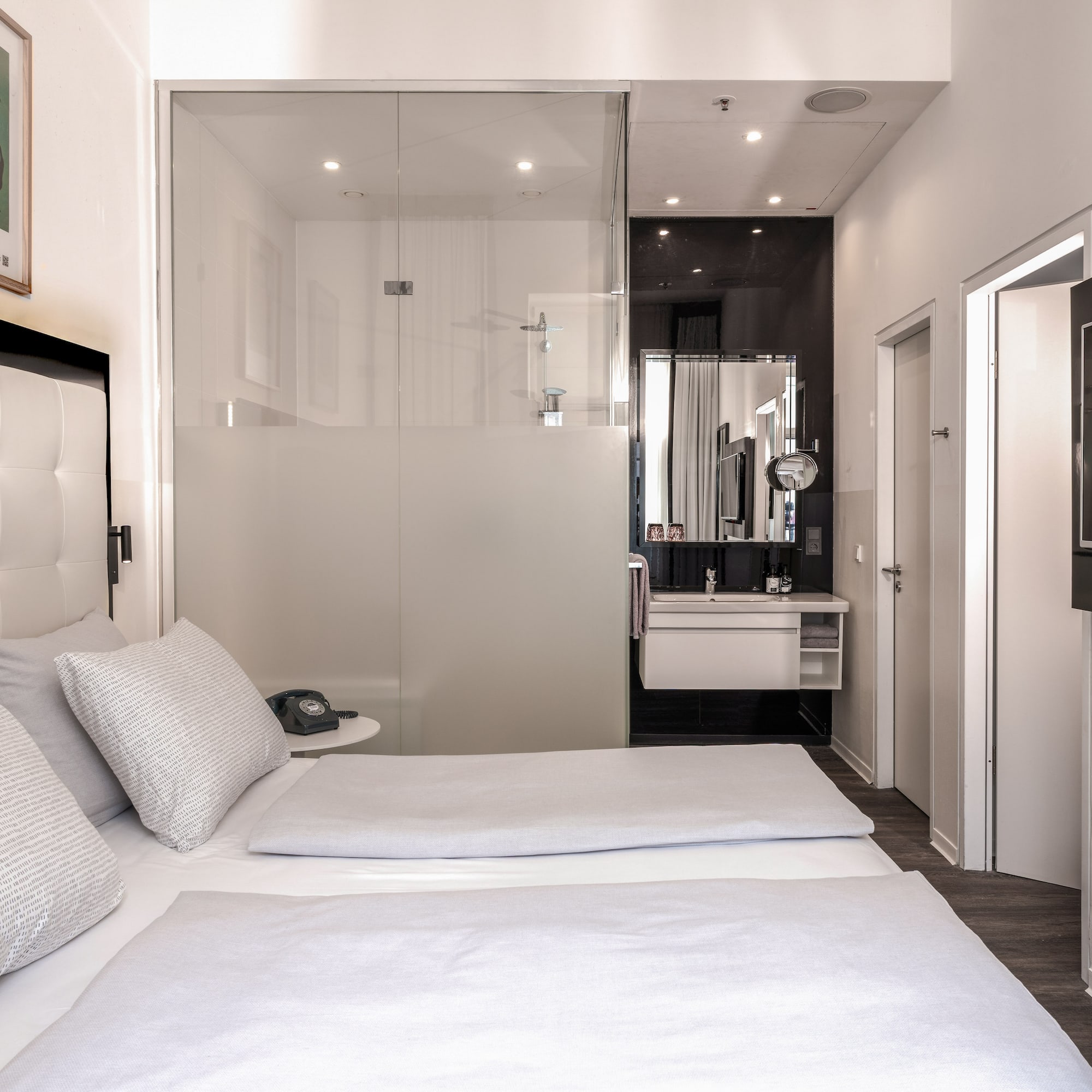 Modern hotel room with twin beds, glass bathroom, and wall-mounted TV.