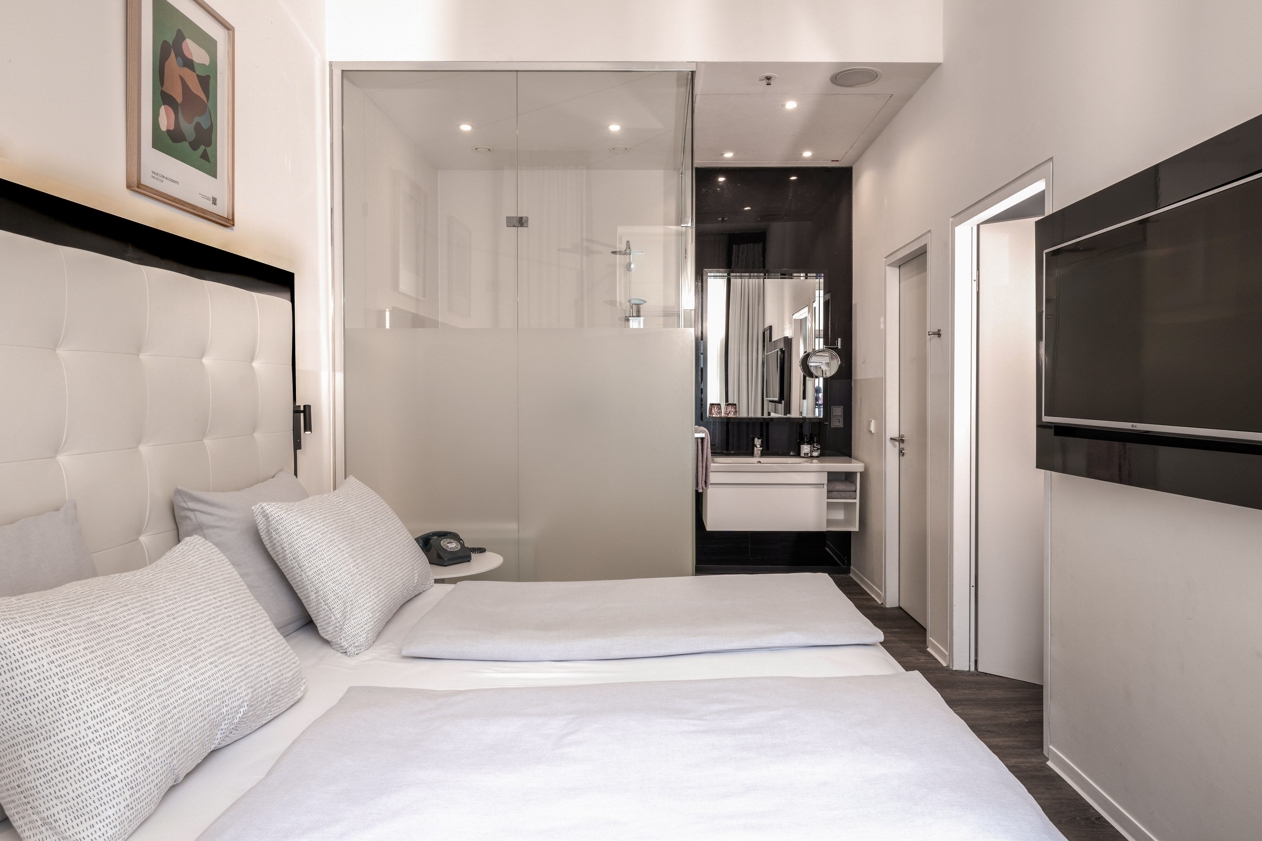 Modern hotel room with twin beds, glass bathroom, and wall-mounted TV.