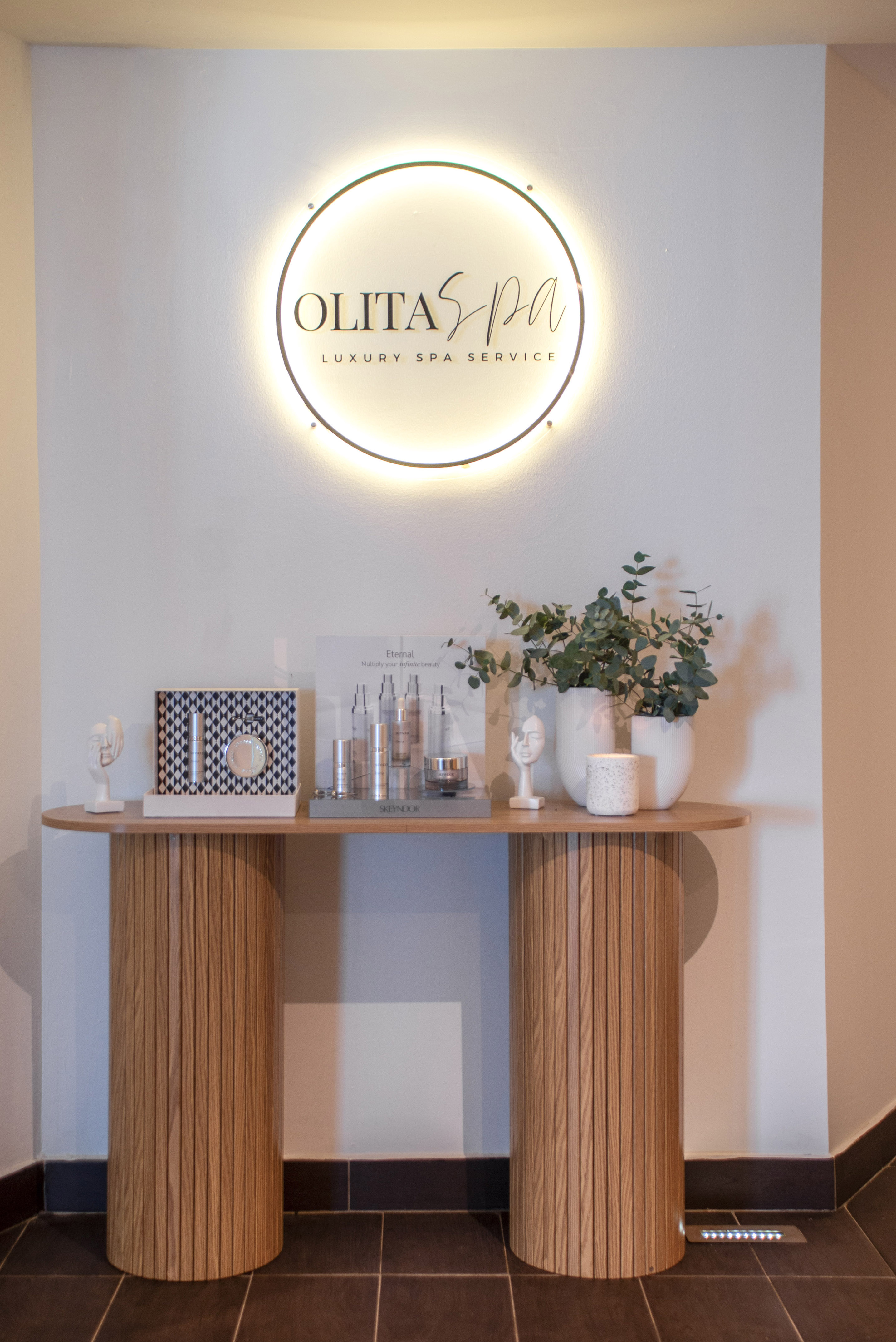 Olitas Spa luxury service illuminated sign, skincare display, plants on console.