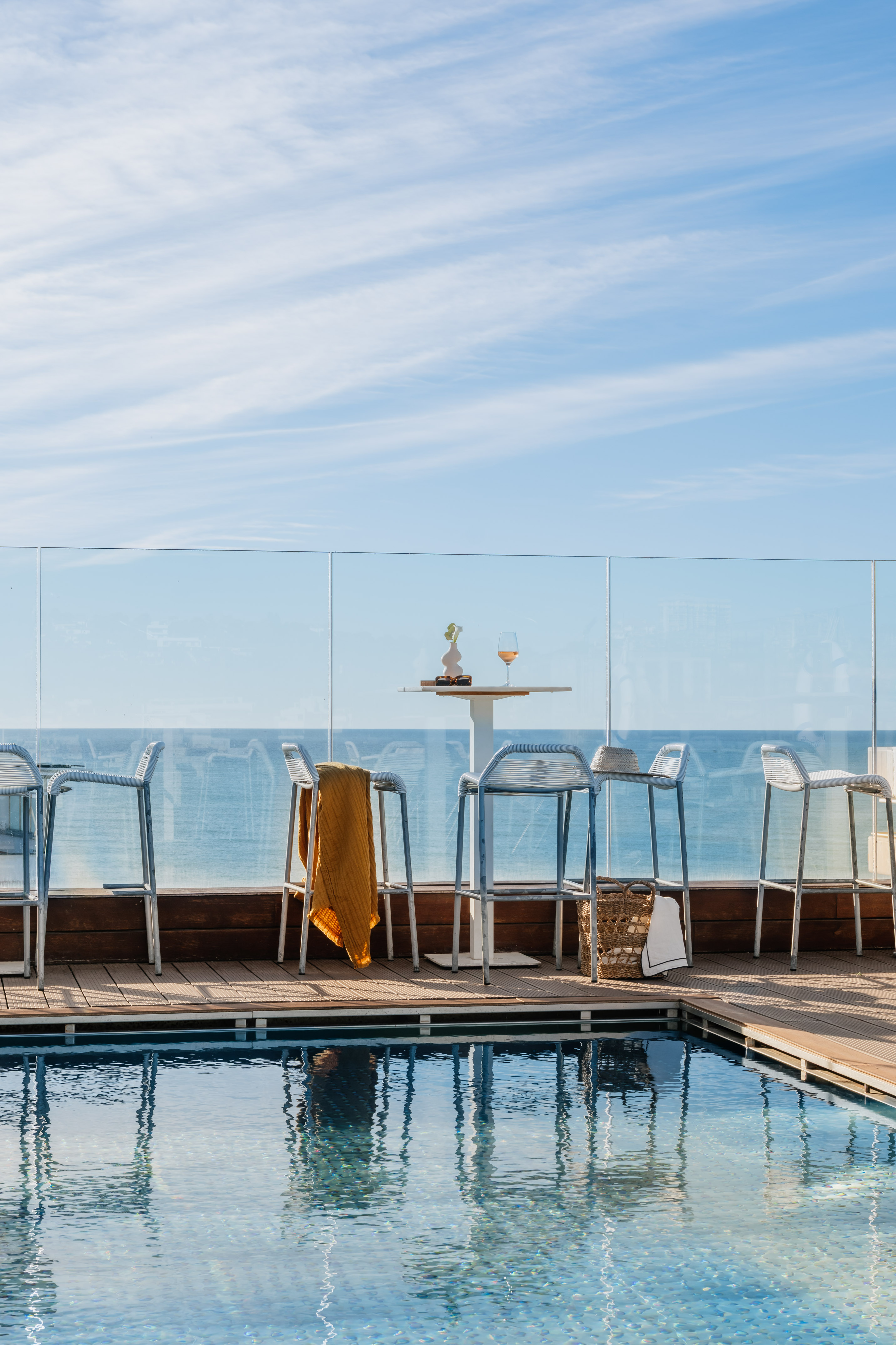Rooftop pool deck with ocean view, bar stools, and a refreshing drink.