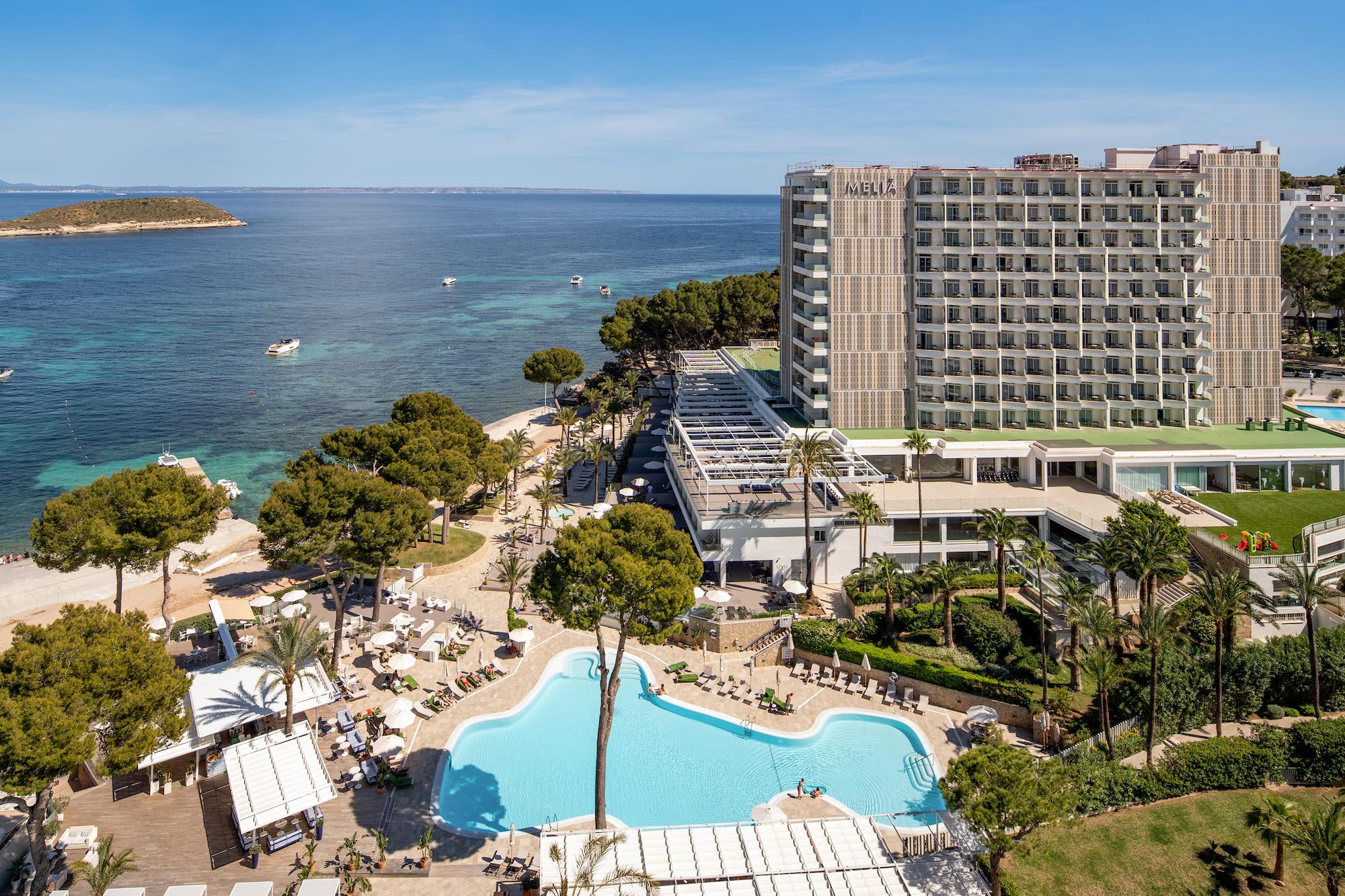 Meliá resort hotel with large pool, beach, blue ocean, boats, and island.