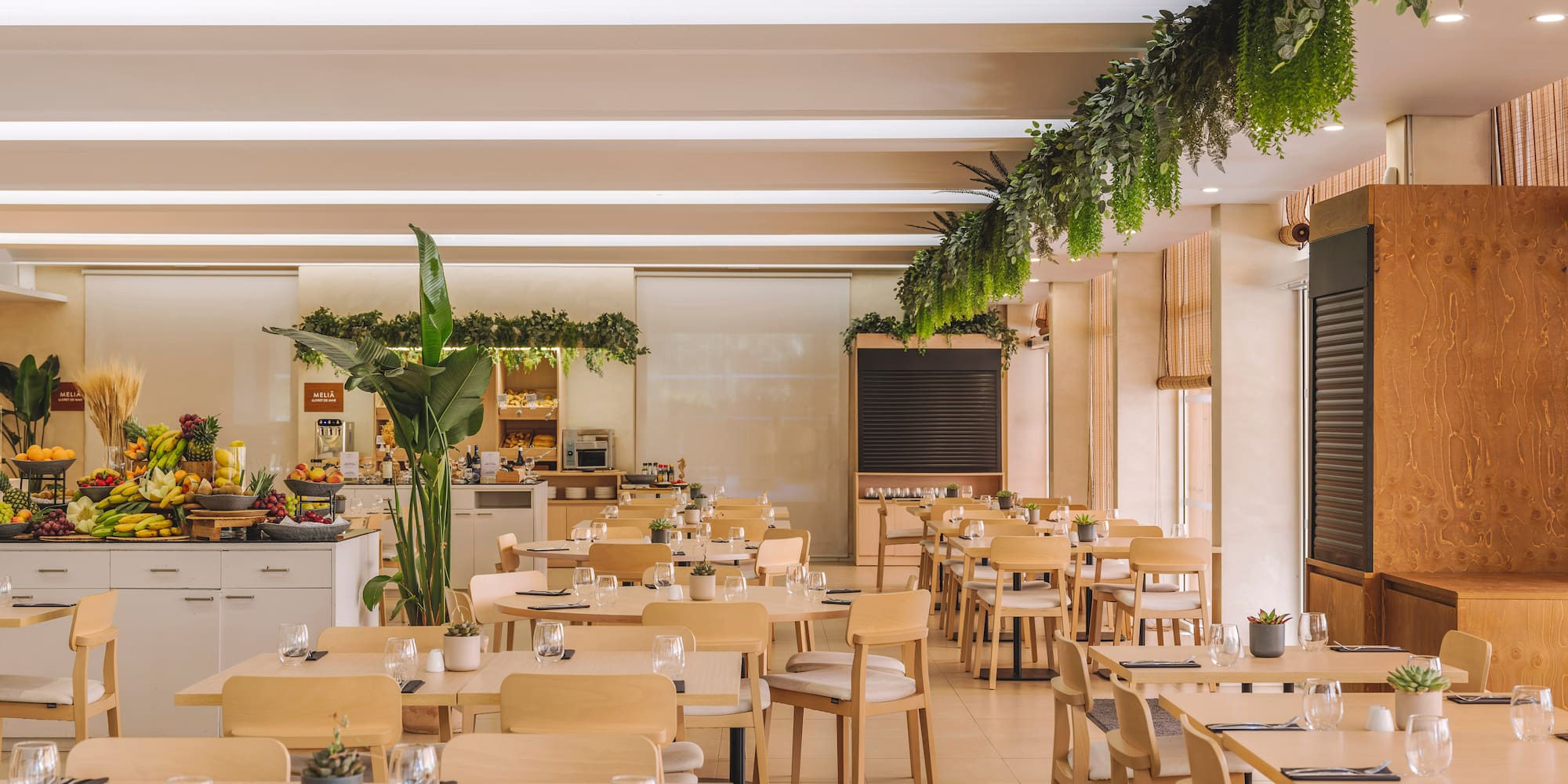 Modern hotel restaurant with buffet, wooden tables, and hanging plants.