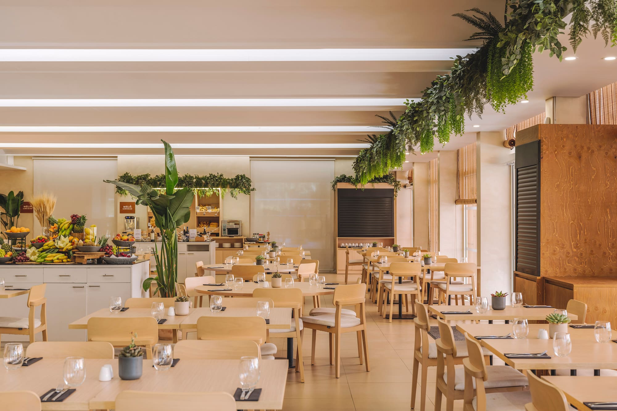 Modern hotel restaurant with buffet, wooden tables, and hanging plants.