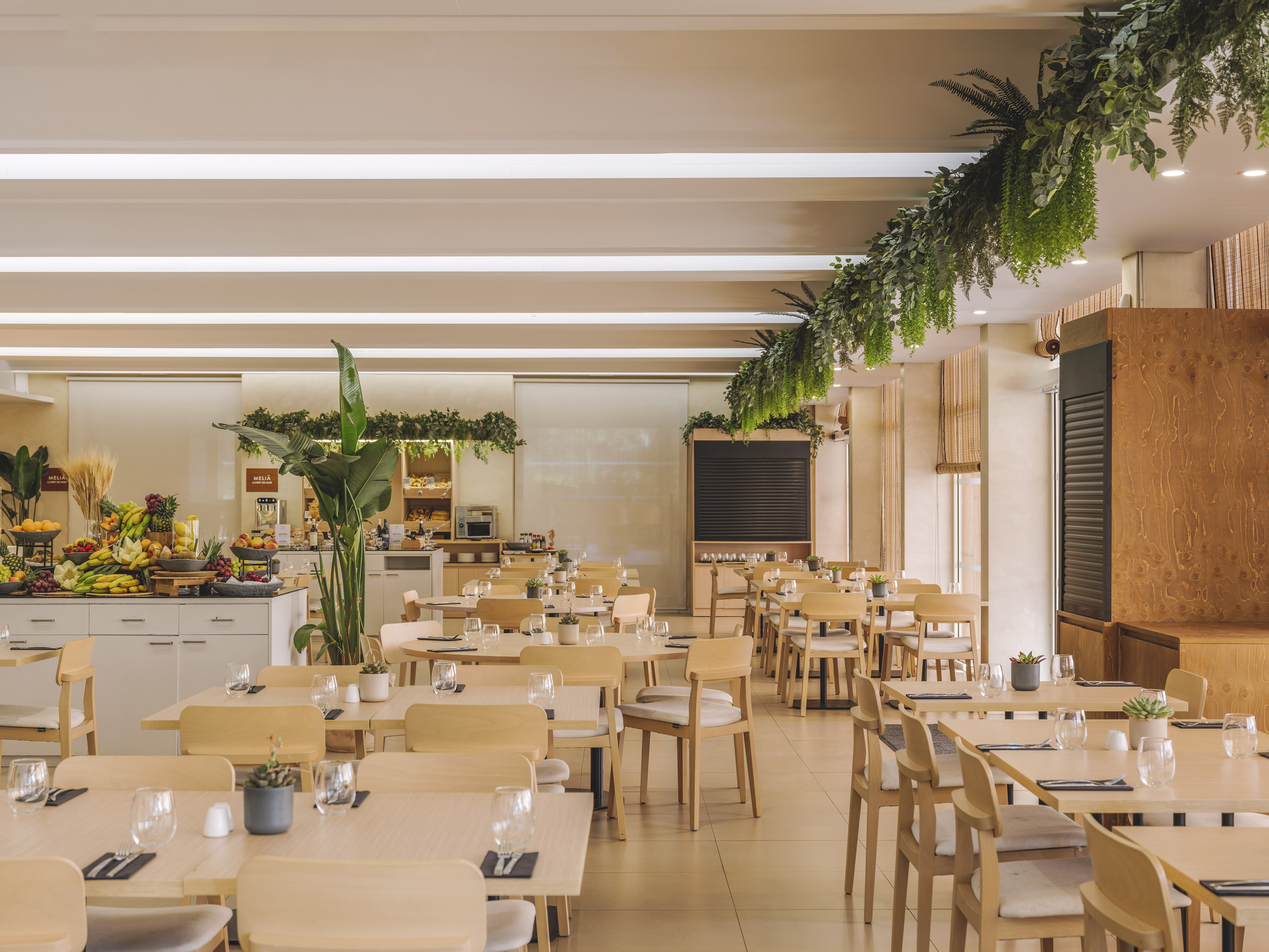 Modern hotel restaurant with buffet, wooden tables, and hanging plants.