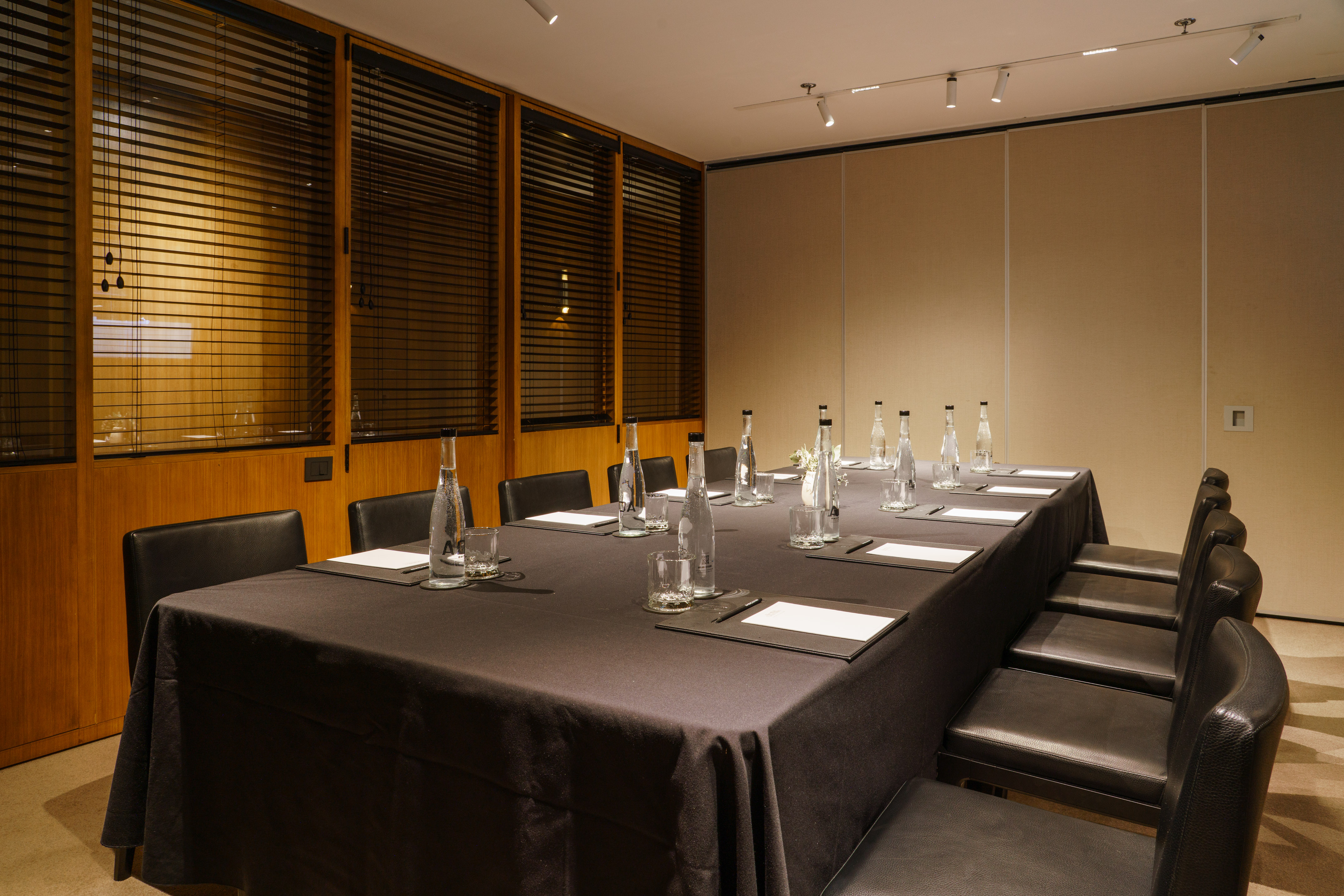 Professional meeting room with dark table, leather chairs, water, and blinds.