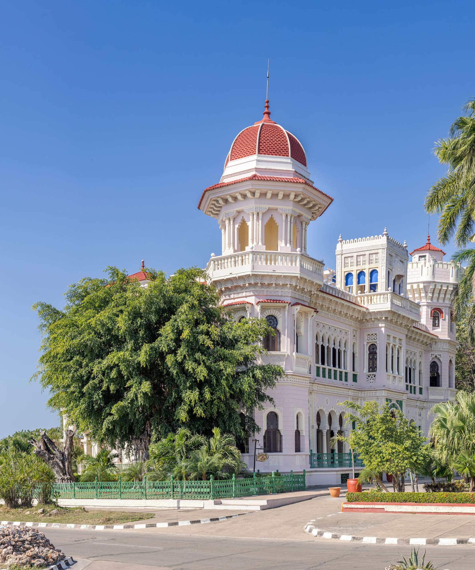 a white building with a red dome and trees with Cienfuegos in the background