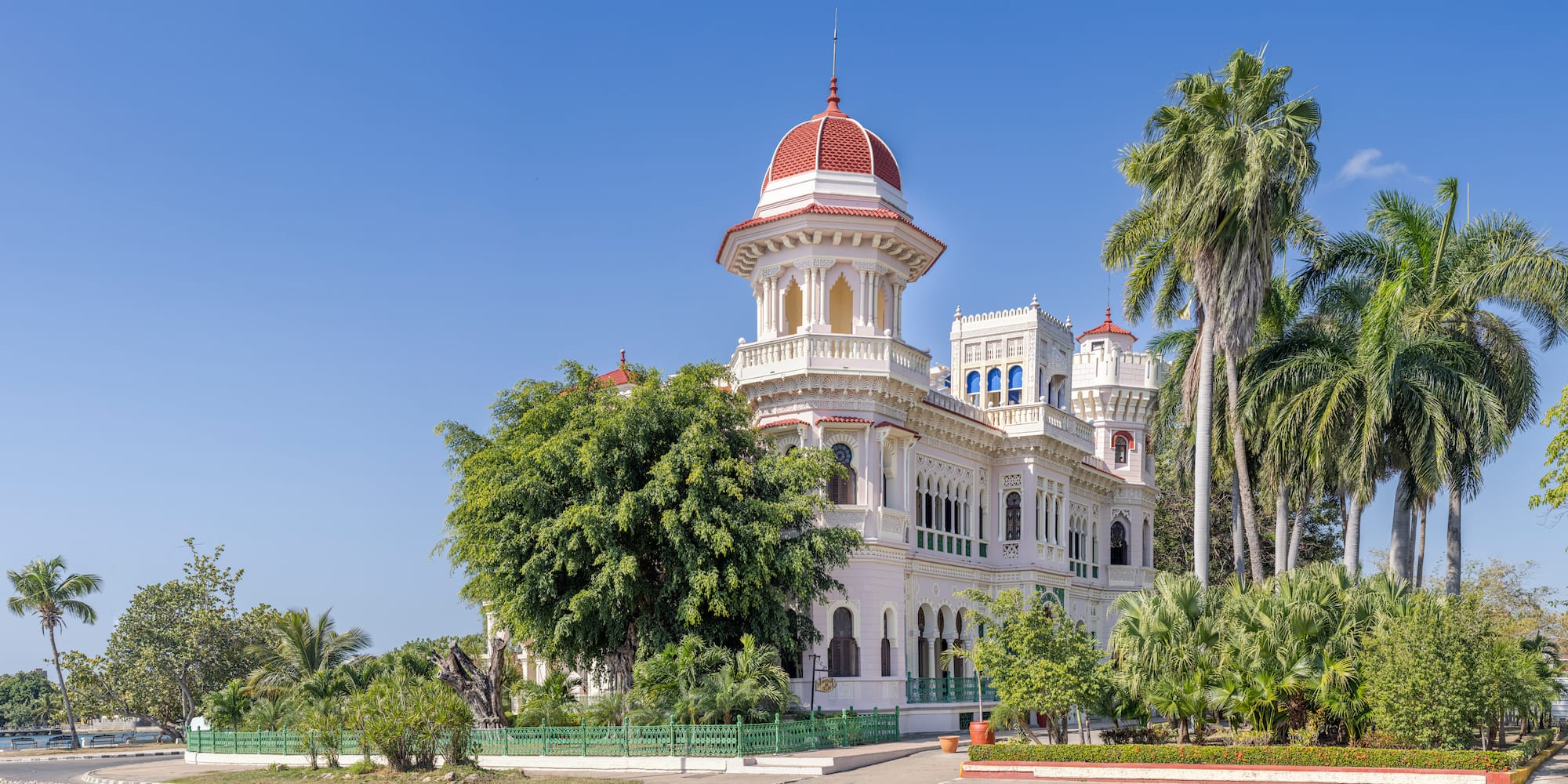 a white building with a red dome and trees with Cienfuegos in the background