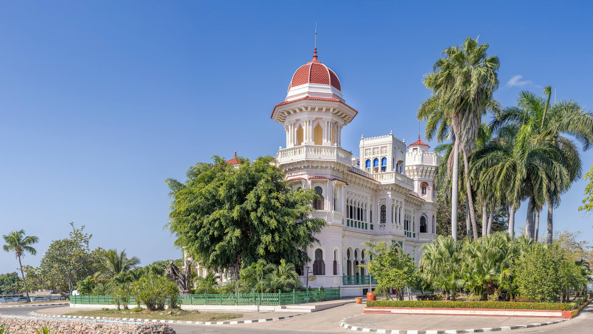 a white building with a red dome and trees with Cienfuegos in the background