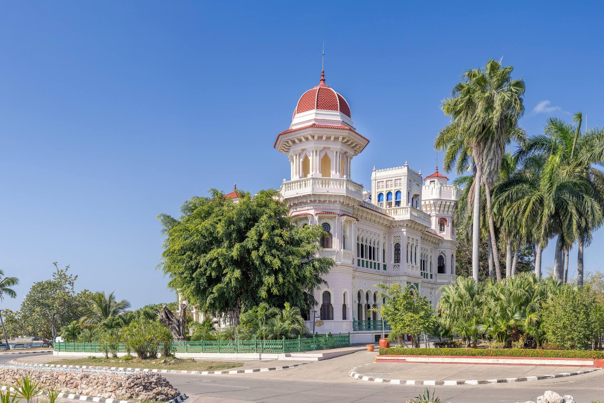 a white building with a red dome and trees with Cienfuegos in the background