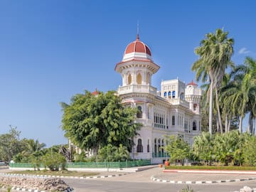 a white building with a red dome and trees with Cienfuegos in the background