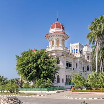 a white building with a red dome and trees with Cienfuegos in the background