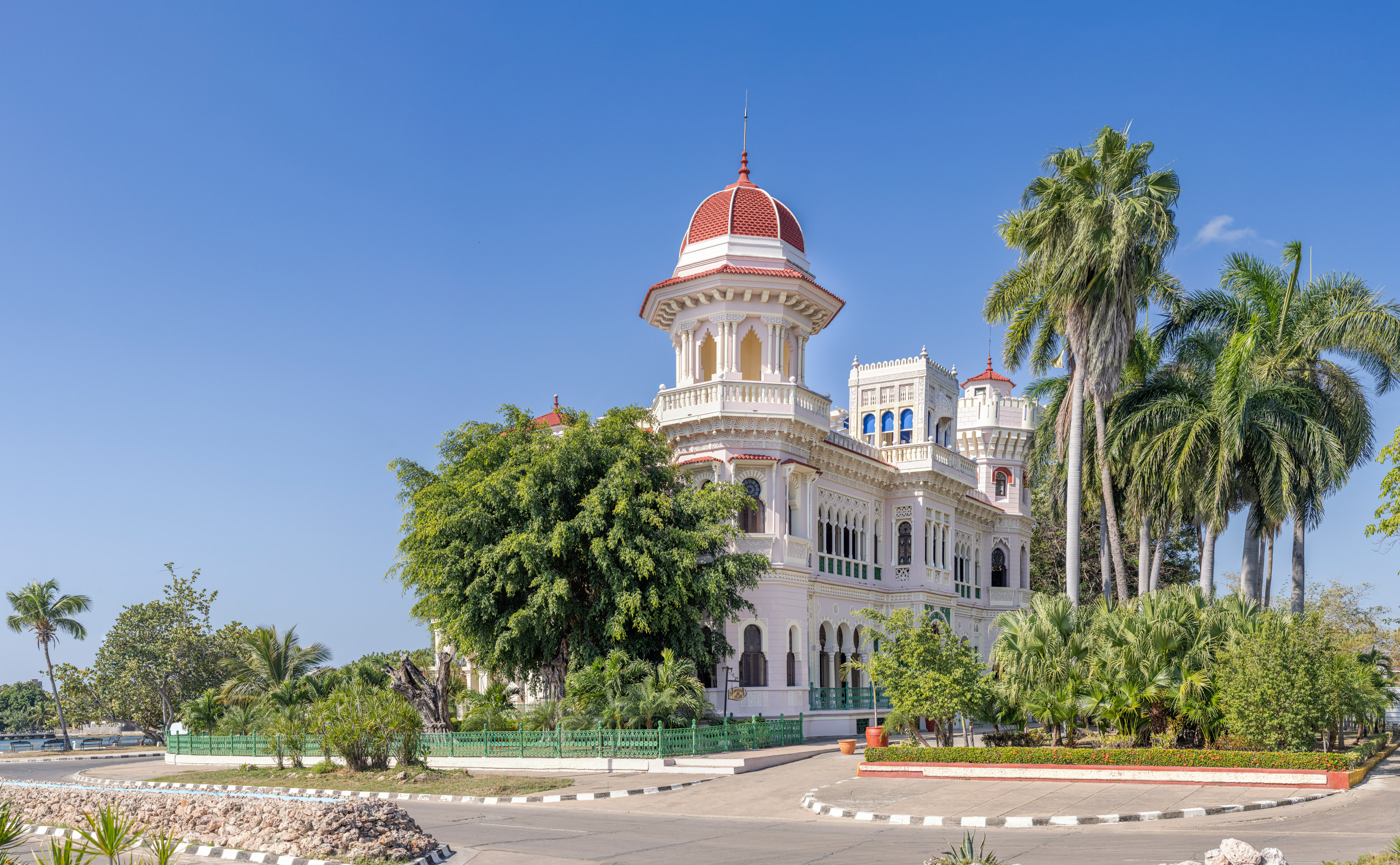 a white building with a red dome and trees with Cienfuegos in the background